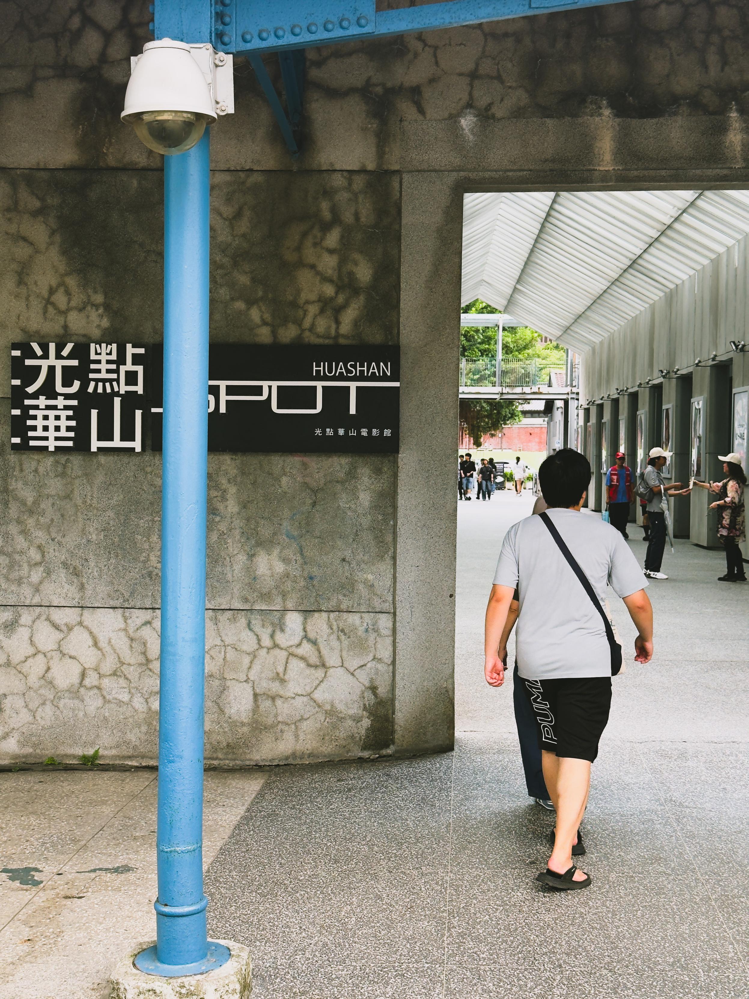 People walking near the entrance of Huashan, a popular mountain and cultural site, with some reading displays and others walking through.