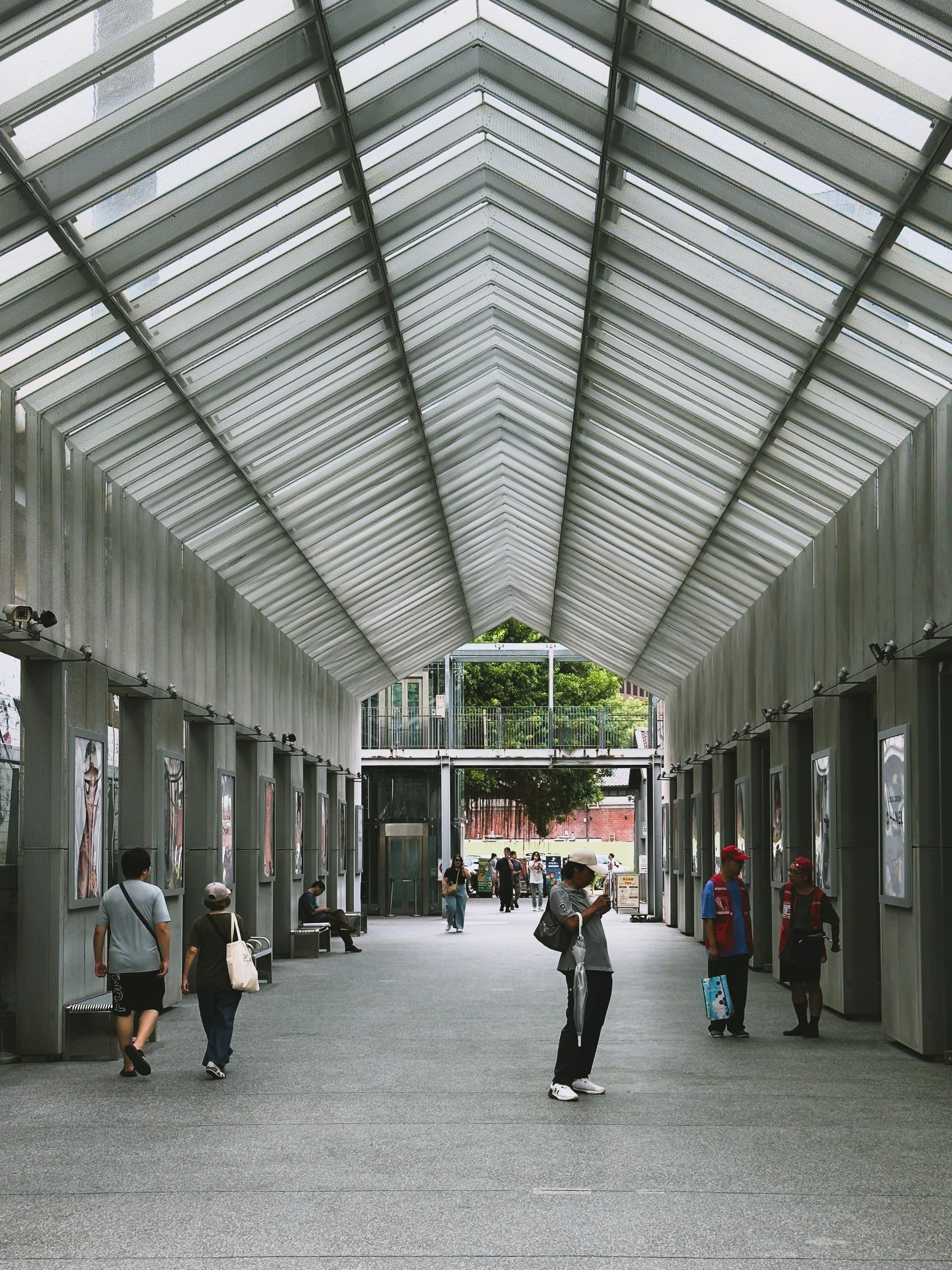 People walking inside a modern, glass-covered walkway with artwork on the walls.