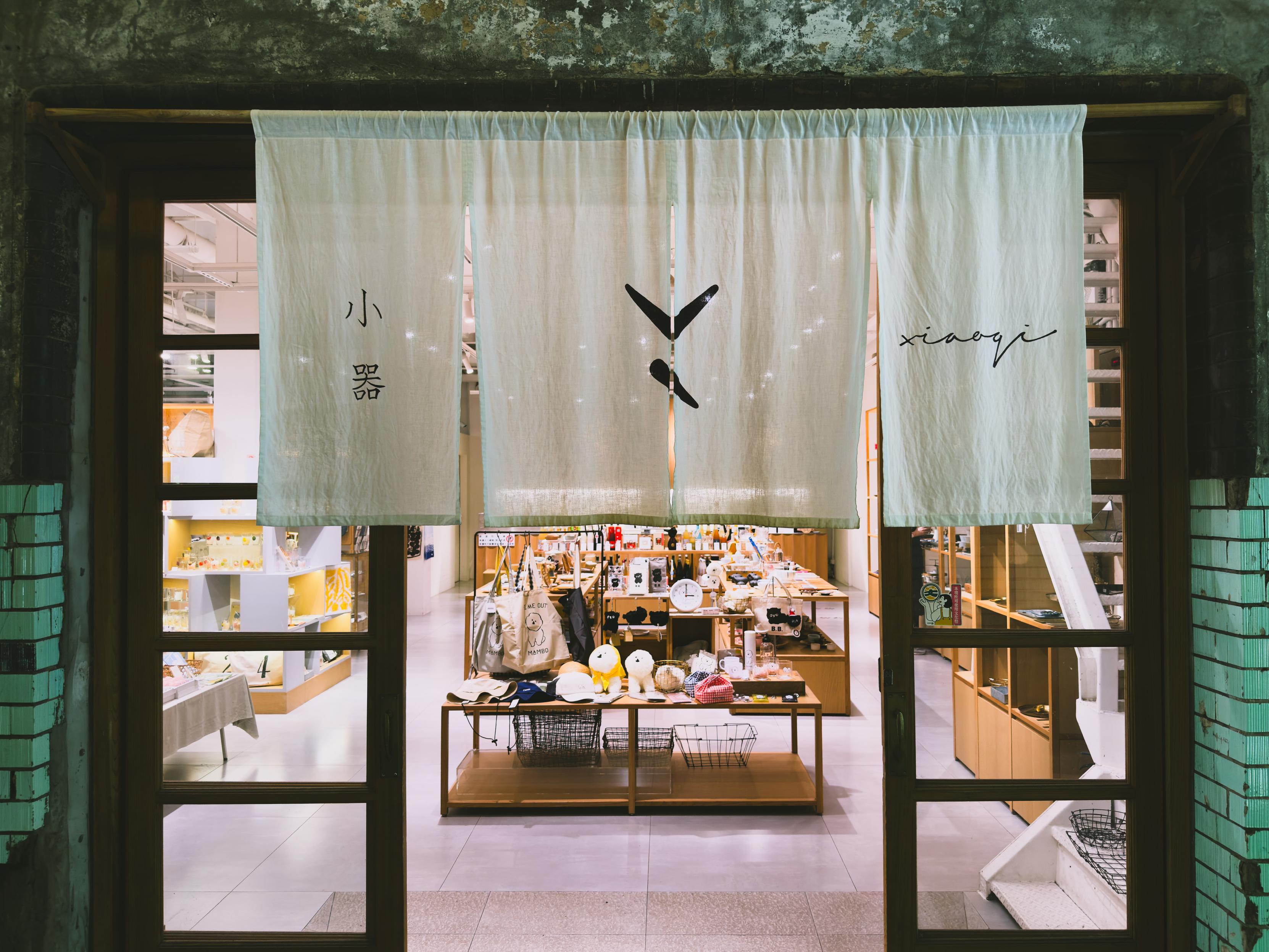 Store entrance with white curtains displaying Chinese characters and the word "xiaoyi," revealing a glimpse of various items inside.