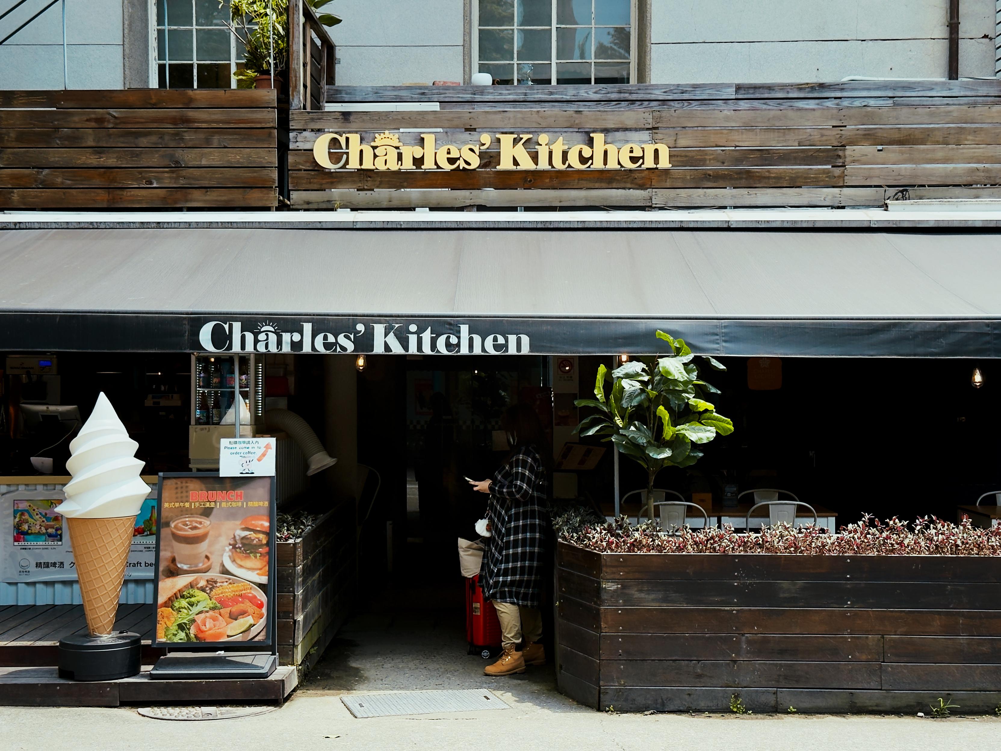Exterior of a restaurant named "Charles' Kitchen" with a large ice cream cone model and a woman standing outside with a suitcase.