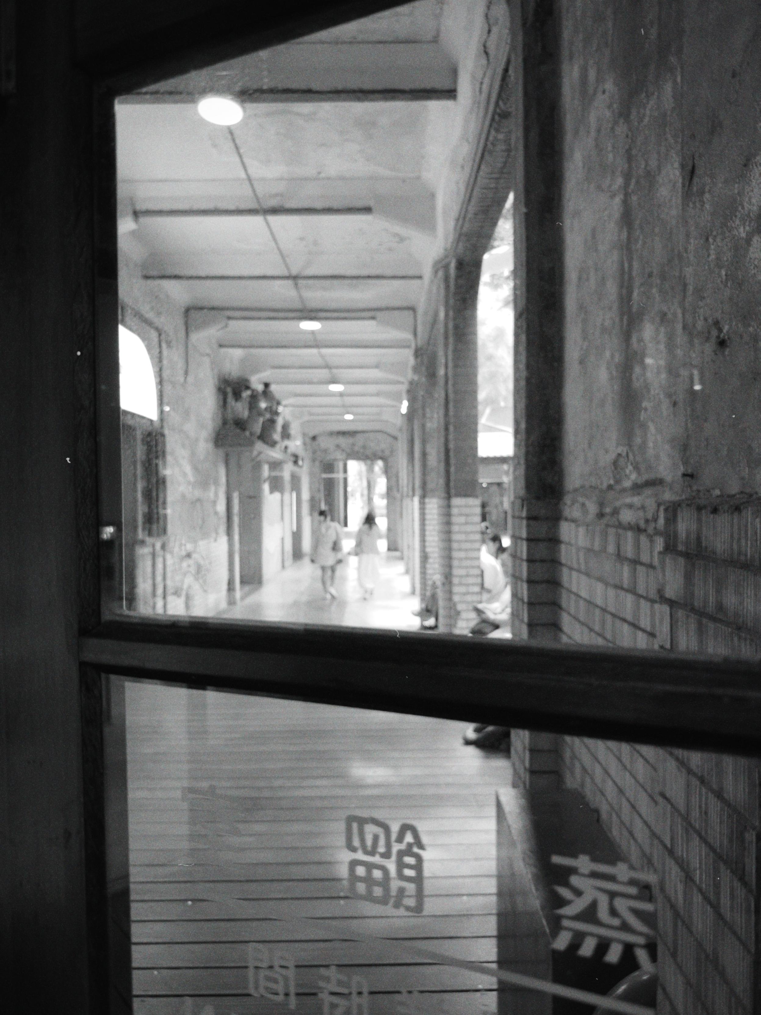 View through a window of an indoor shopping or walking area with people in the distance, brick walls, and ambient lighting.