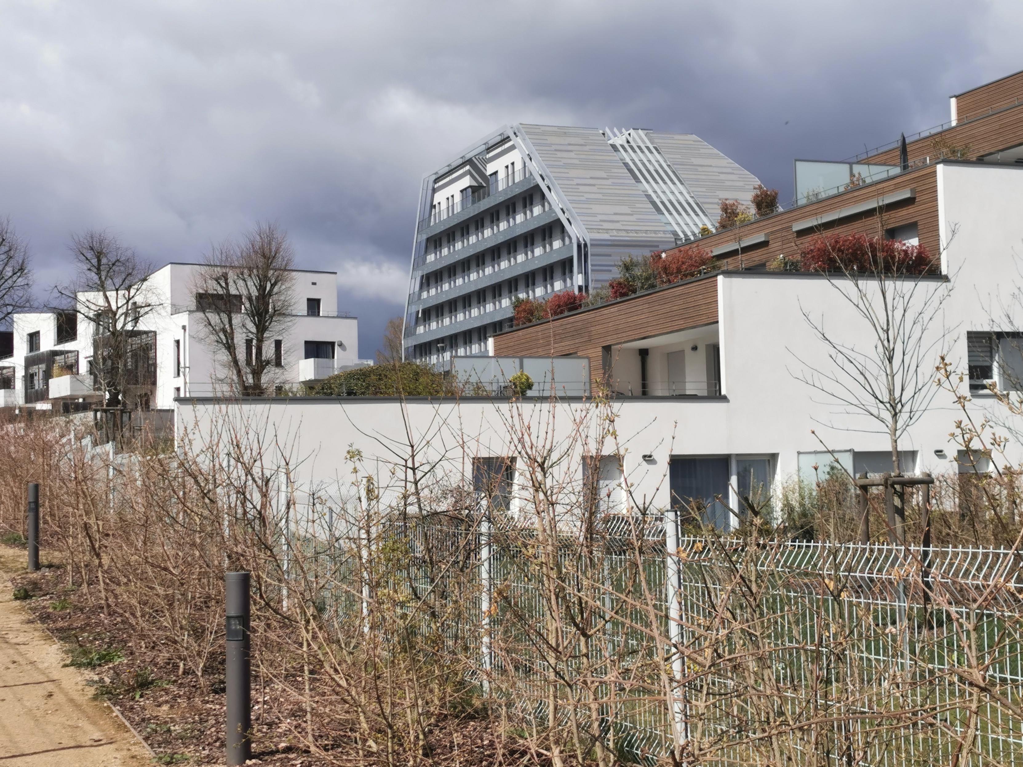 Vue sur un quartier flambant neuf de petits immeubles, avec un immeuble plus original à l'horizon.
