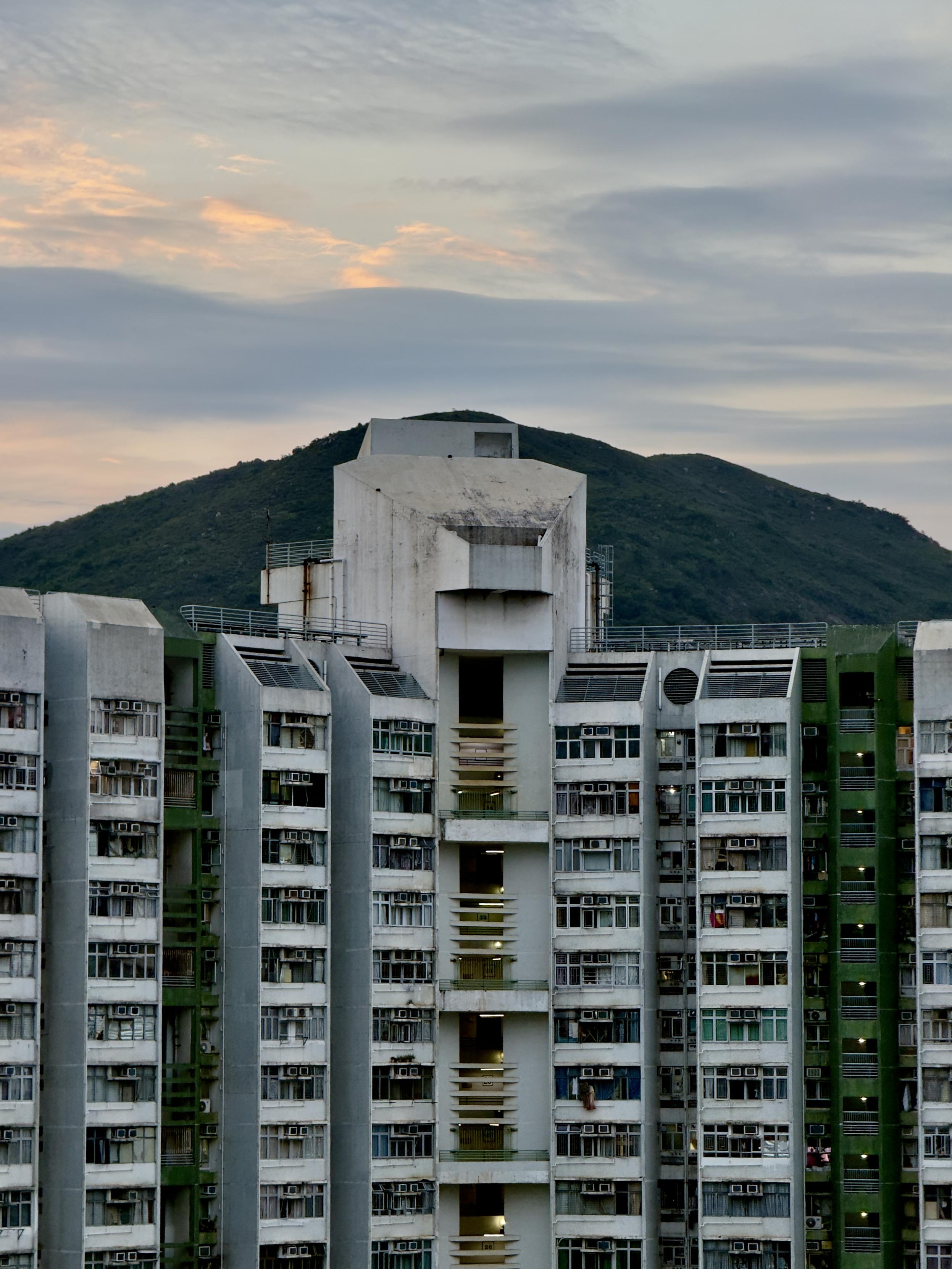 Residential apartment building with mountain and cloudy sky in the background during dusk.