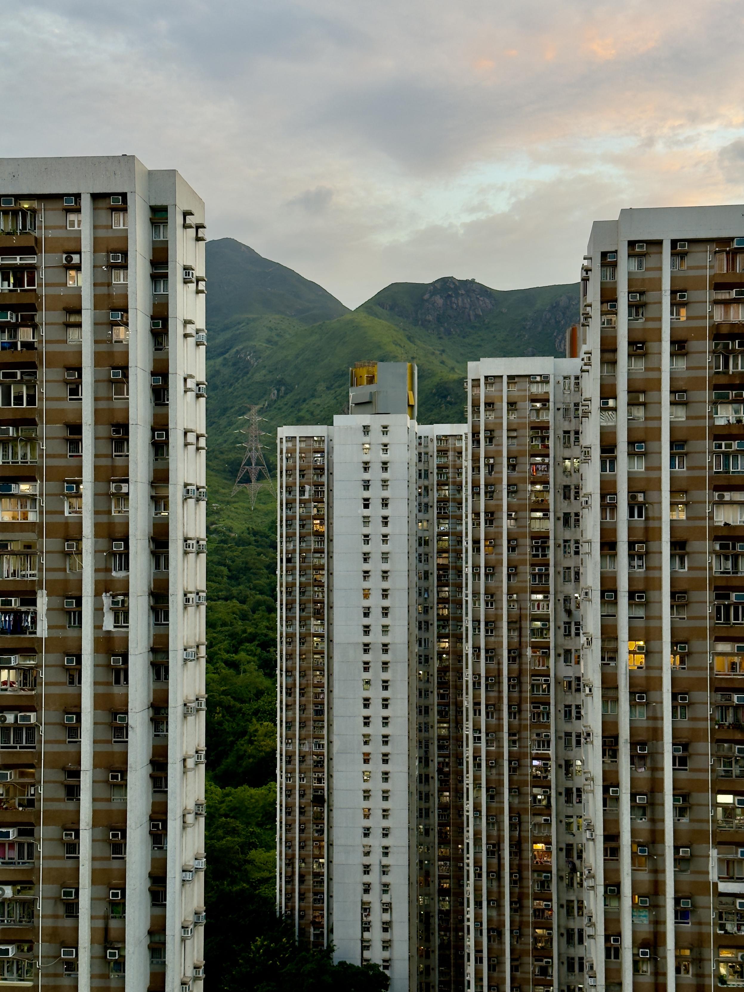 High-rise apartment buildings with green mountains in the background at dusk.