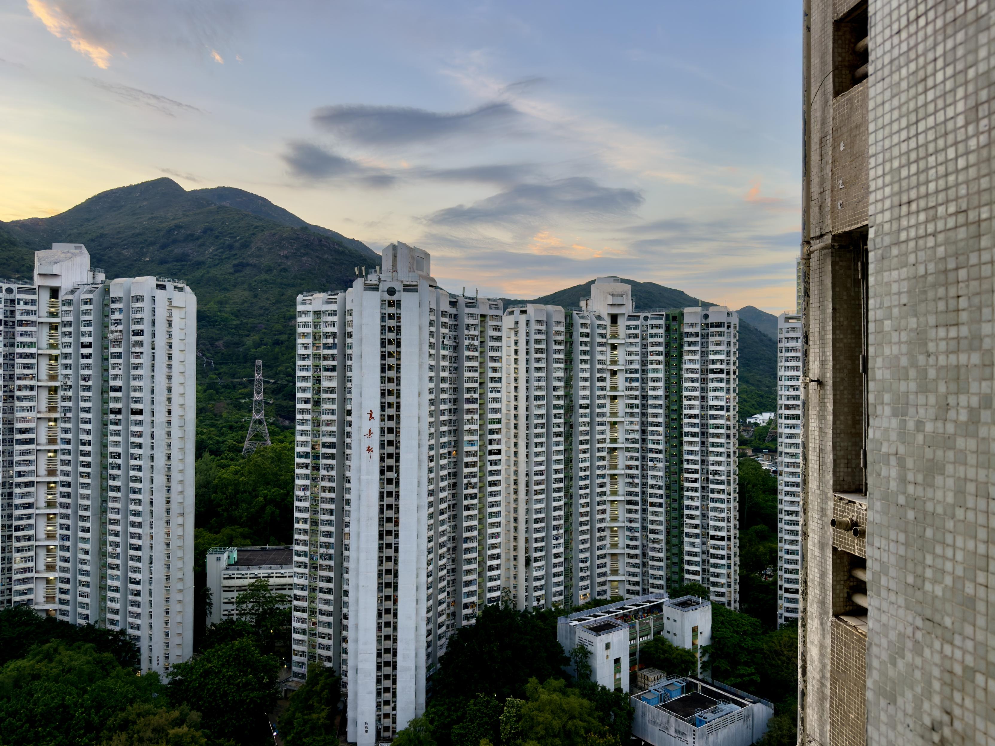 多座高层白色住宅楼环绕绿色山丘，天色渐暗，天空中有云彩。
