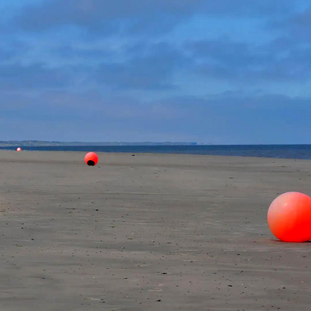 Badestrand auf der Nordseeinsel Spiekeroog bei Ebbe. Auf dem weiten Sandstrand liegen die Bojen auf dem Trockenen. Normalerweise grenzen sie im Wasser den überwachten Badebereich ab. Es ergibt sich ein toller Kontrast aufgrund ihrer hellorangen Farbe und dem grauen Sand. Spiekeroog 2026