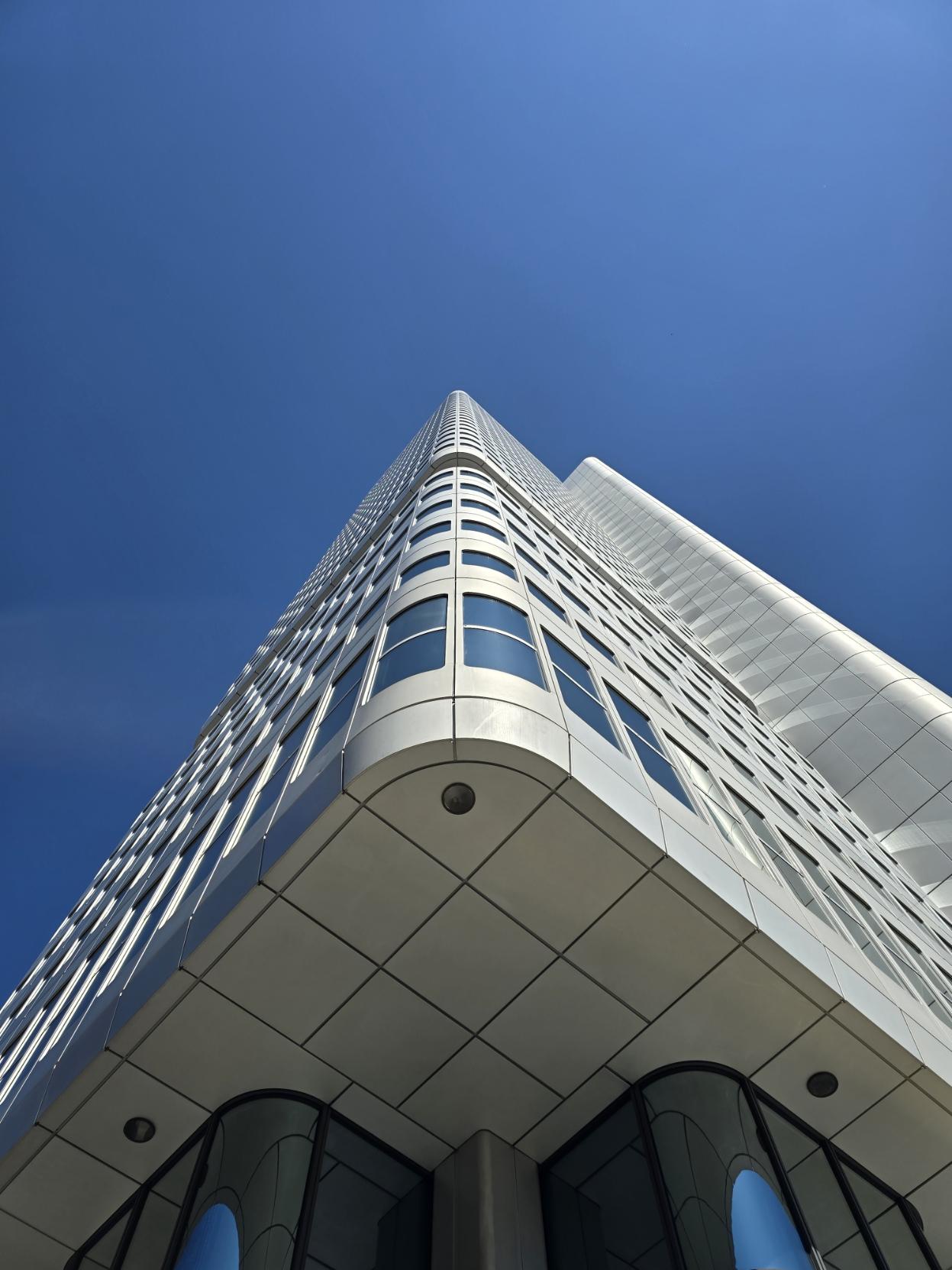 Silbergraues Hochhaus berührt den blauen Himmel.