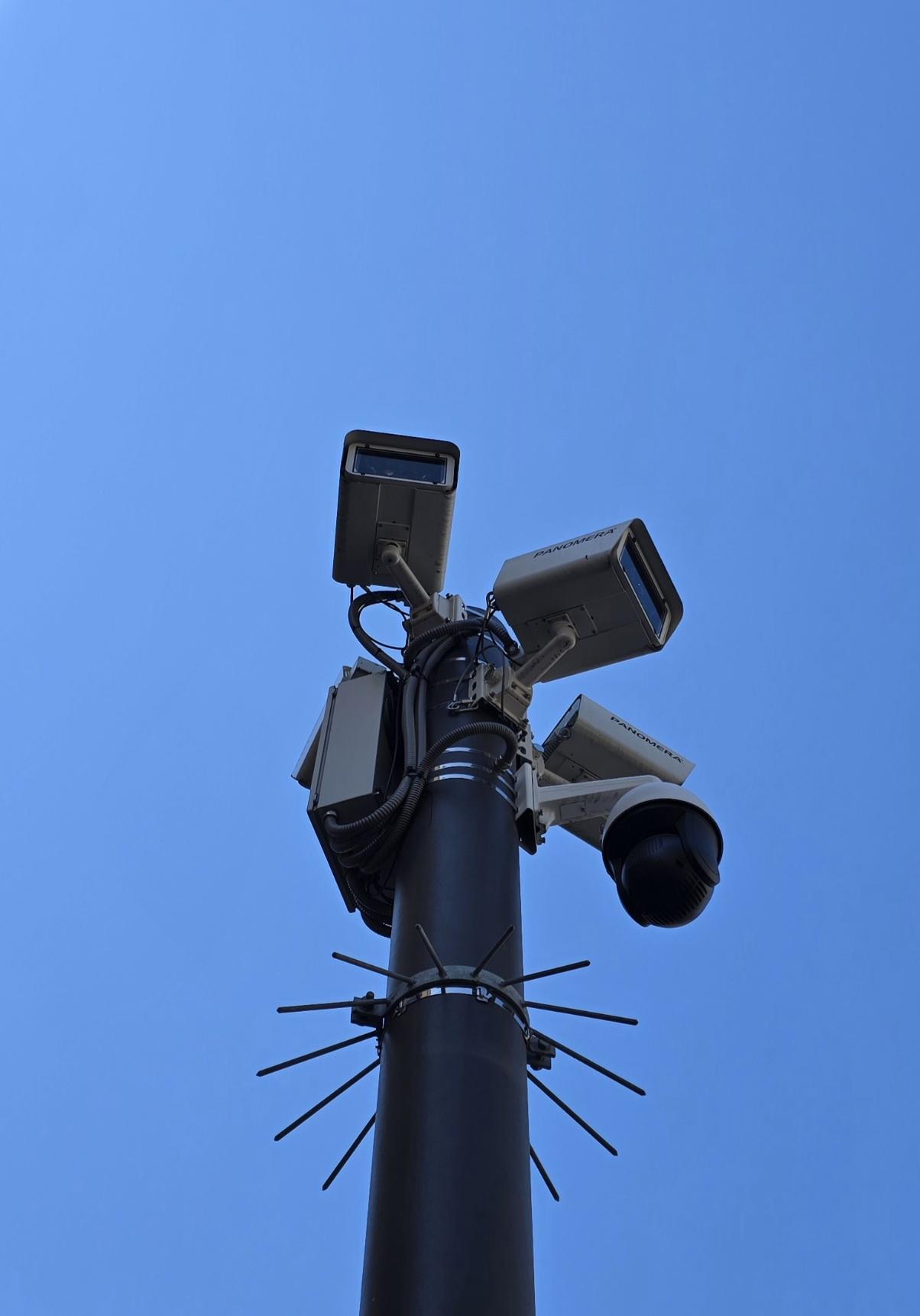 Ein Mast mit vielen Überwachungskameras berührt den blauen Himmel.