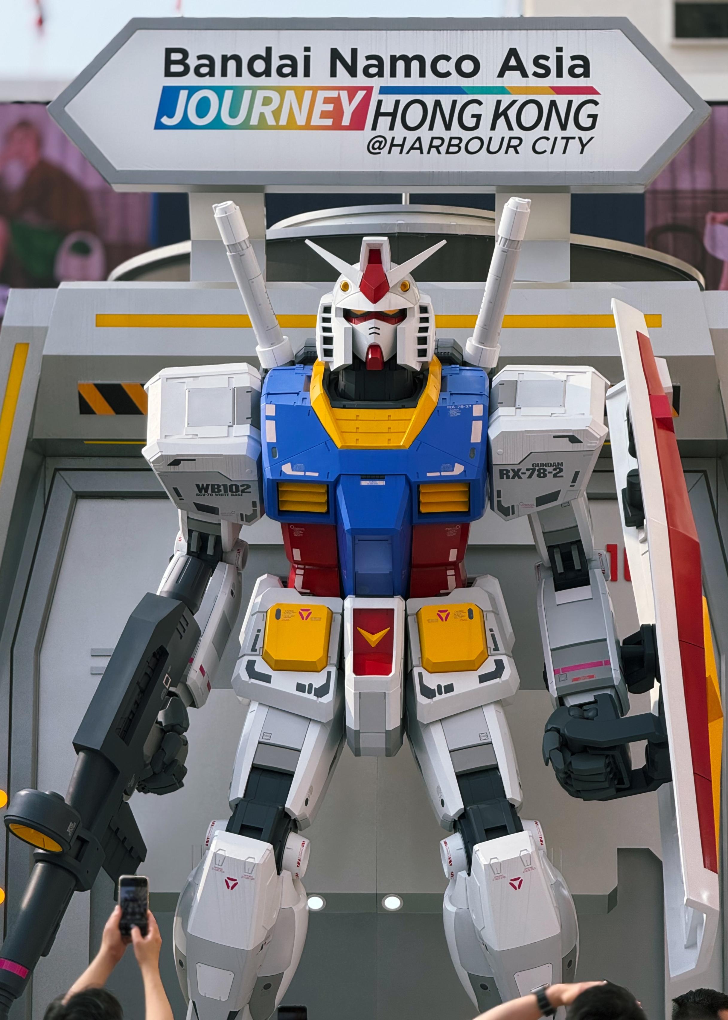 高达模型展示在展览中，背后有“Bandai Namco Asia”标牌，许多观众用手机拍照。