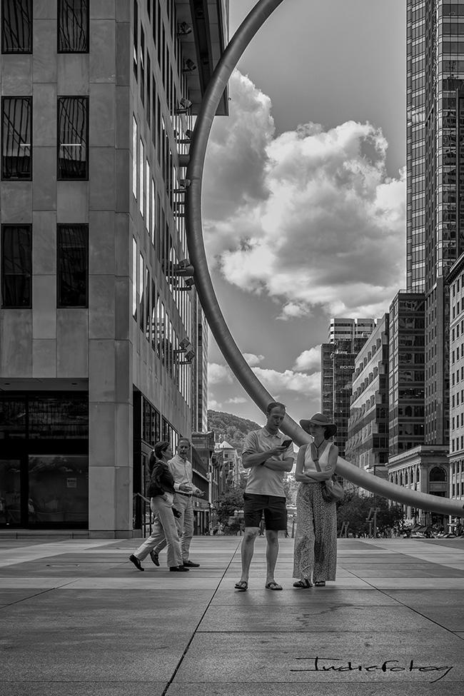 A couple posing in front of a huge ring sculpture, with people passing by.