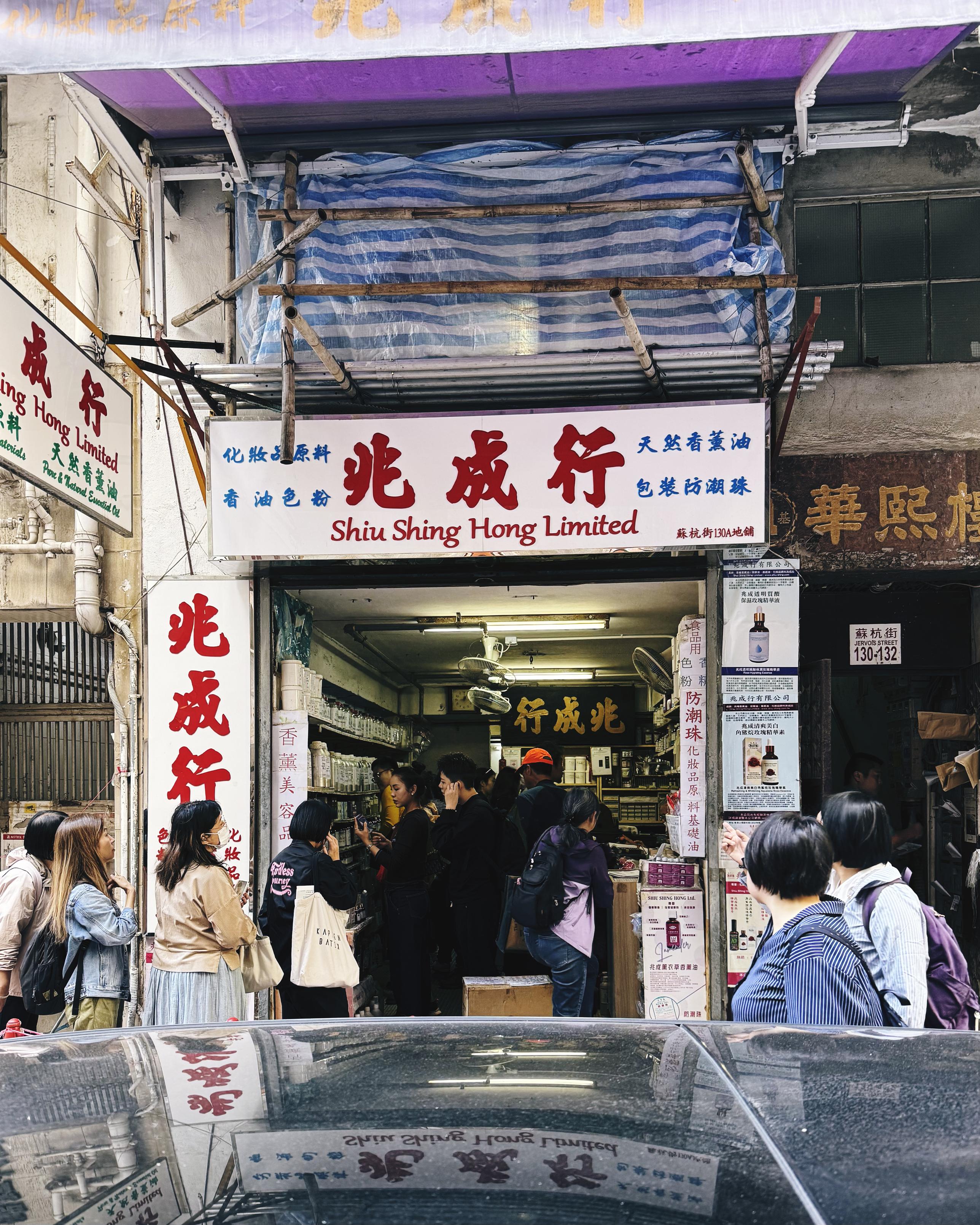 店铺门口人们排队等待，招牌写着“兆成行 Shiu Shing Hong Limited”。