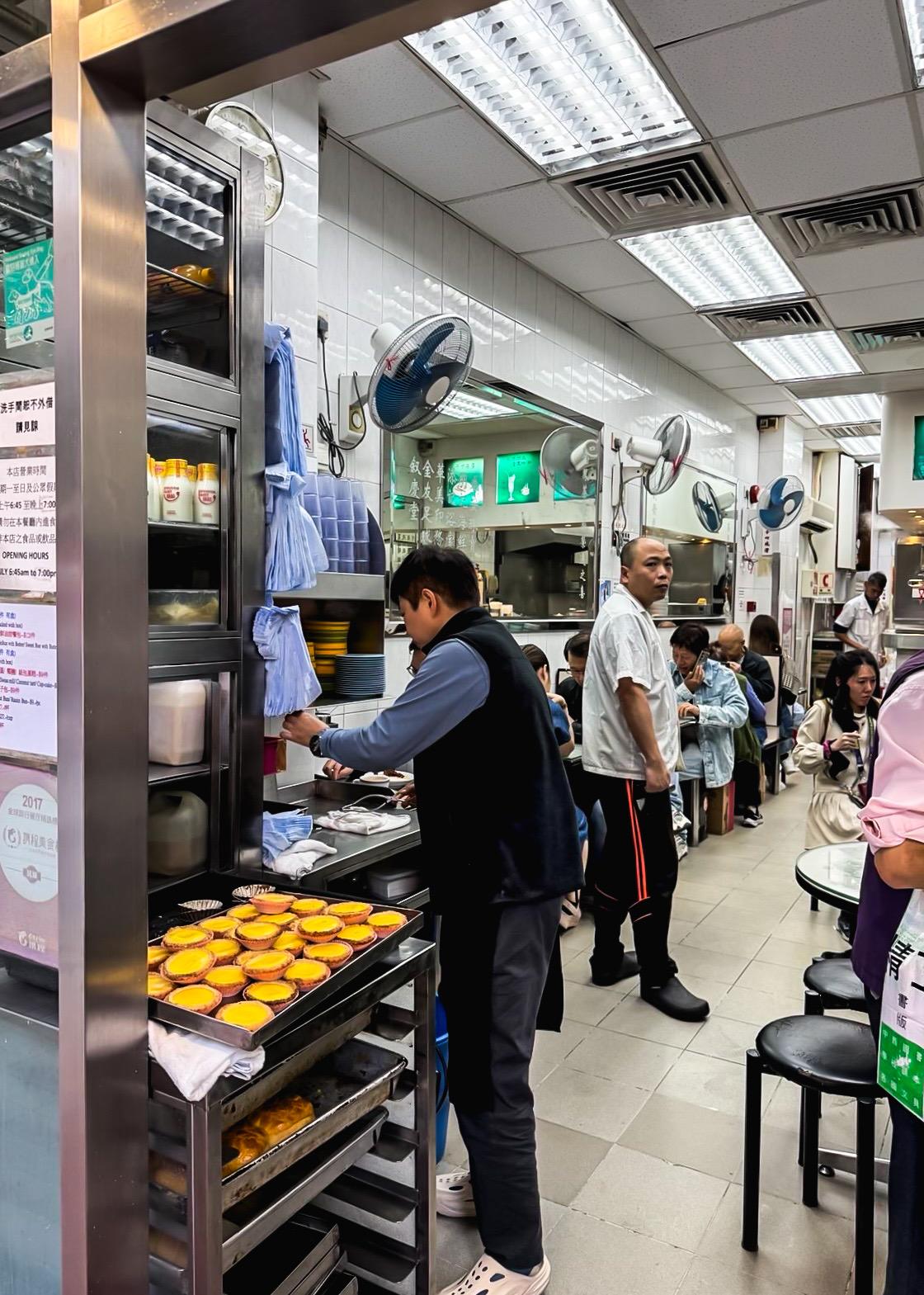 繁忙的餐厅内，厨师准备甜点，餐客排队等待，氛围热闹。