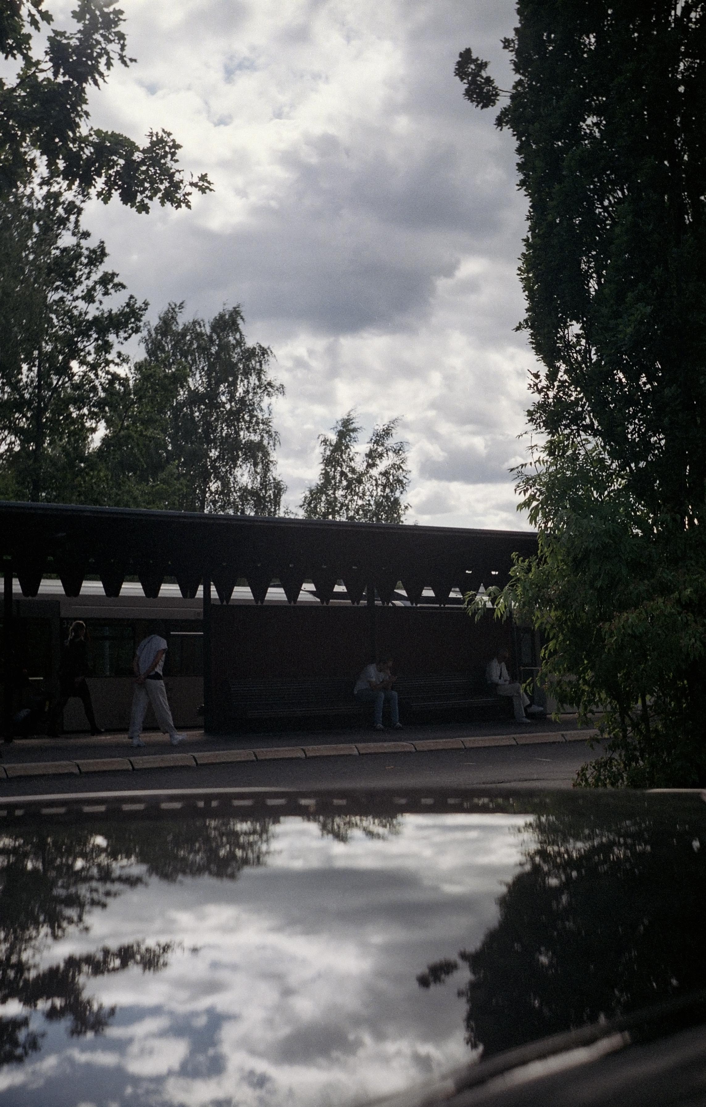 Dark, cloudy sky over a metro platform. The sky and trees reflecting in a car roof.