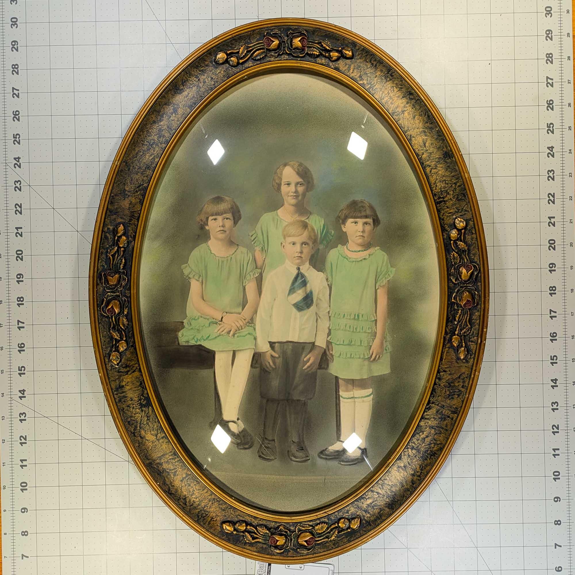 Crayon portrait of 4 children in a decorative antique bubble glass frame
3 girls and one younger boy in the center
The boy is wearing a very short and wide necktie which looks like it could possibly be a handkerchief