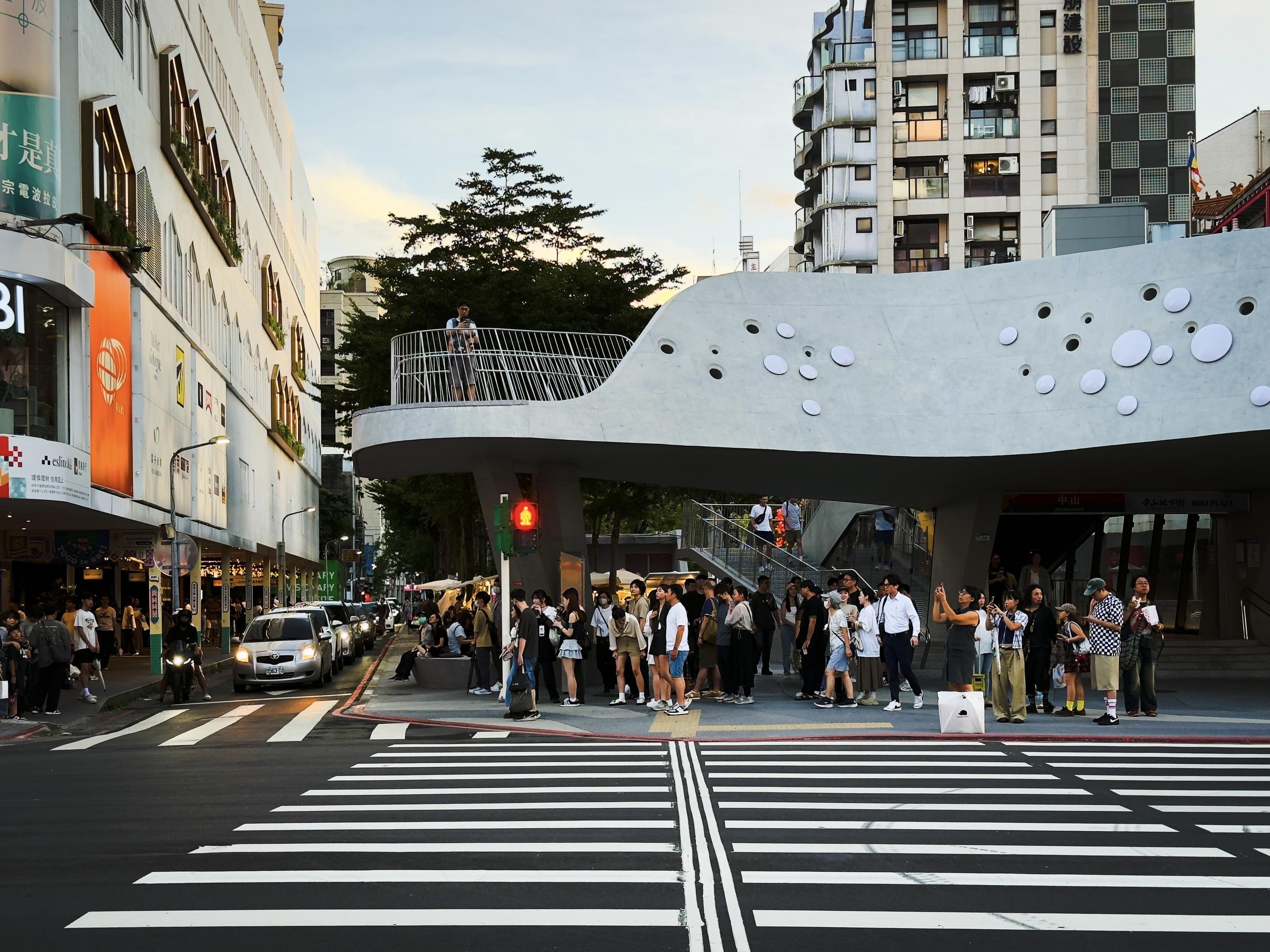 繁忙的街头人们排队等候，背景是现代建筑和一座独特的建筑物，天色渐暗。