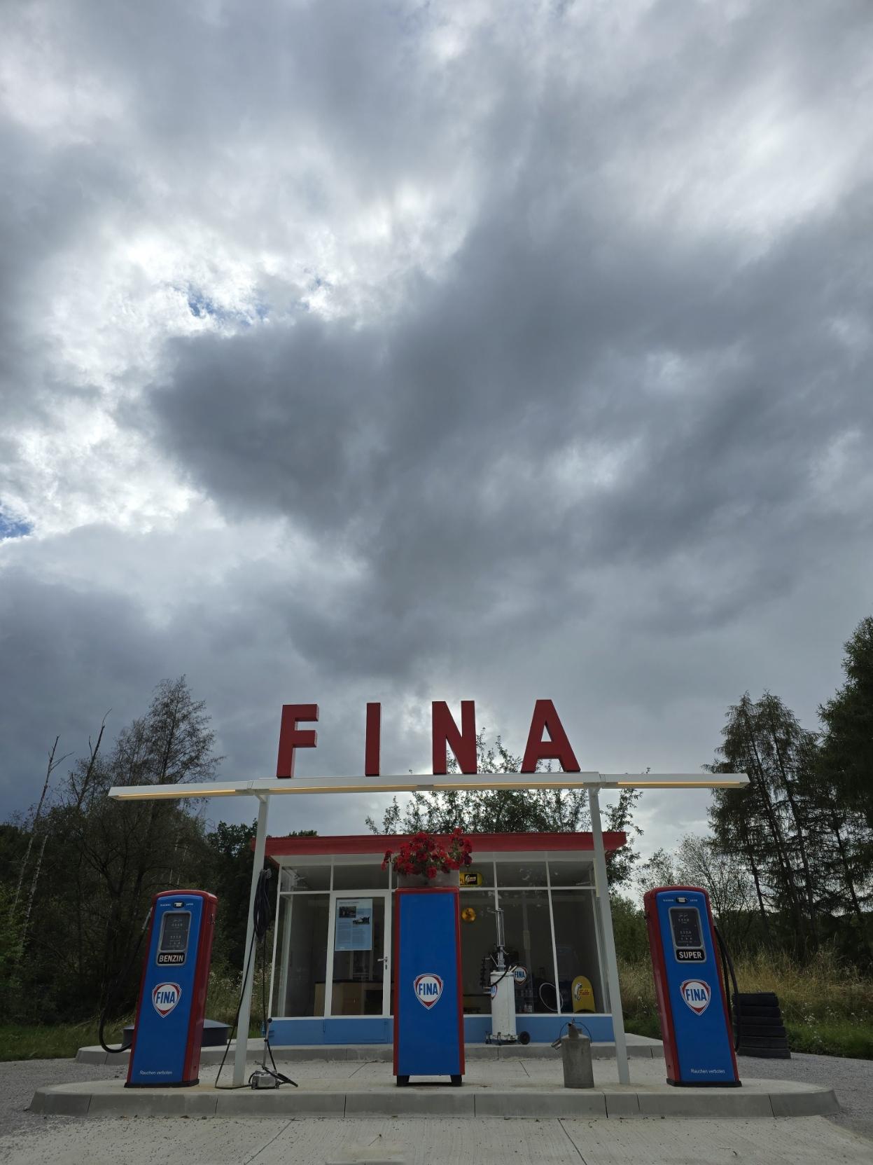 In color. A gas station from 1959. The word “Fina” in the center. Above it, clouds, some with rain.