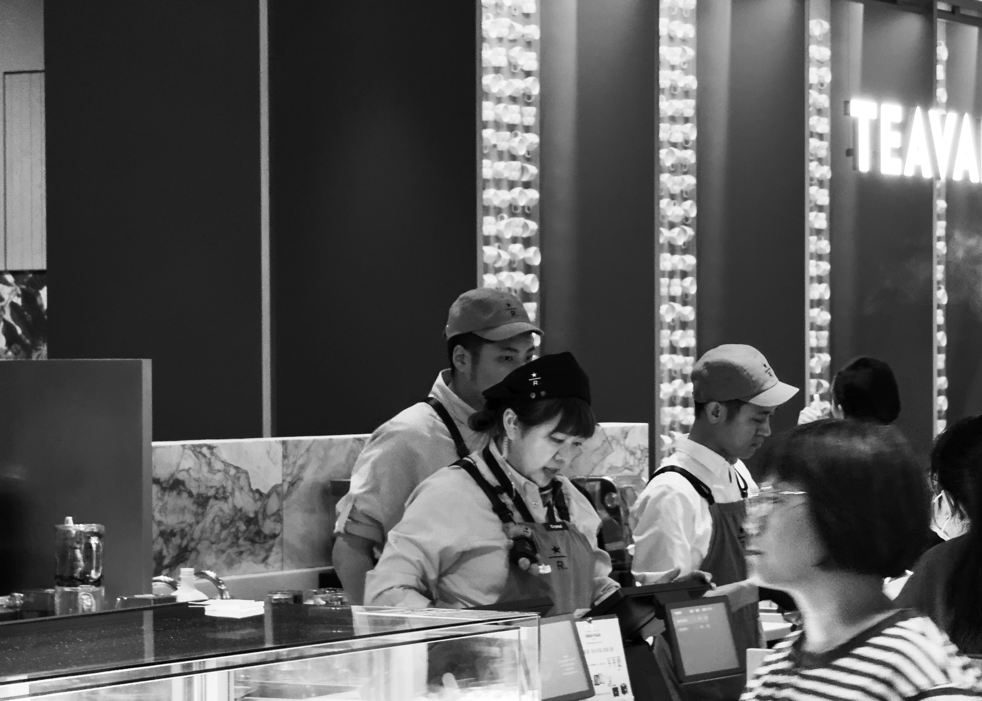 超市工作人员在收银台前工作，背景有"TEAVANA"标识。