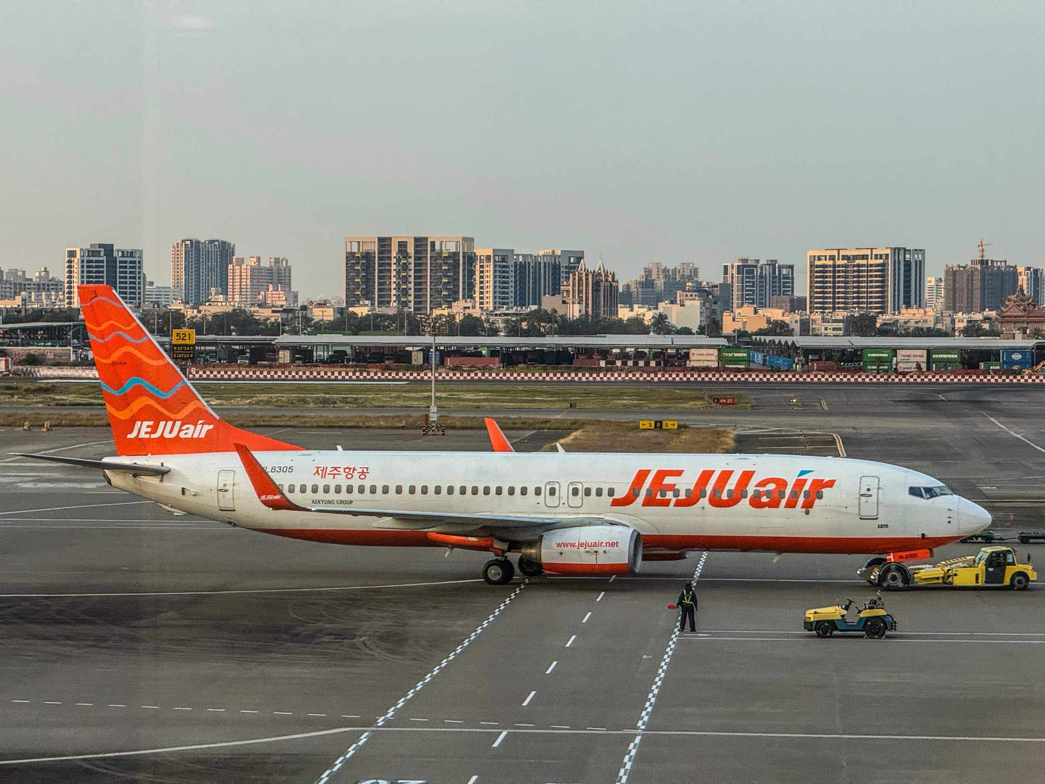 濟州航空的白色與橙色飛機停靠在跑道上，背景是城市的高樓大廈。