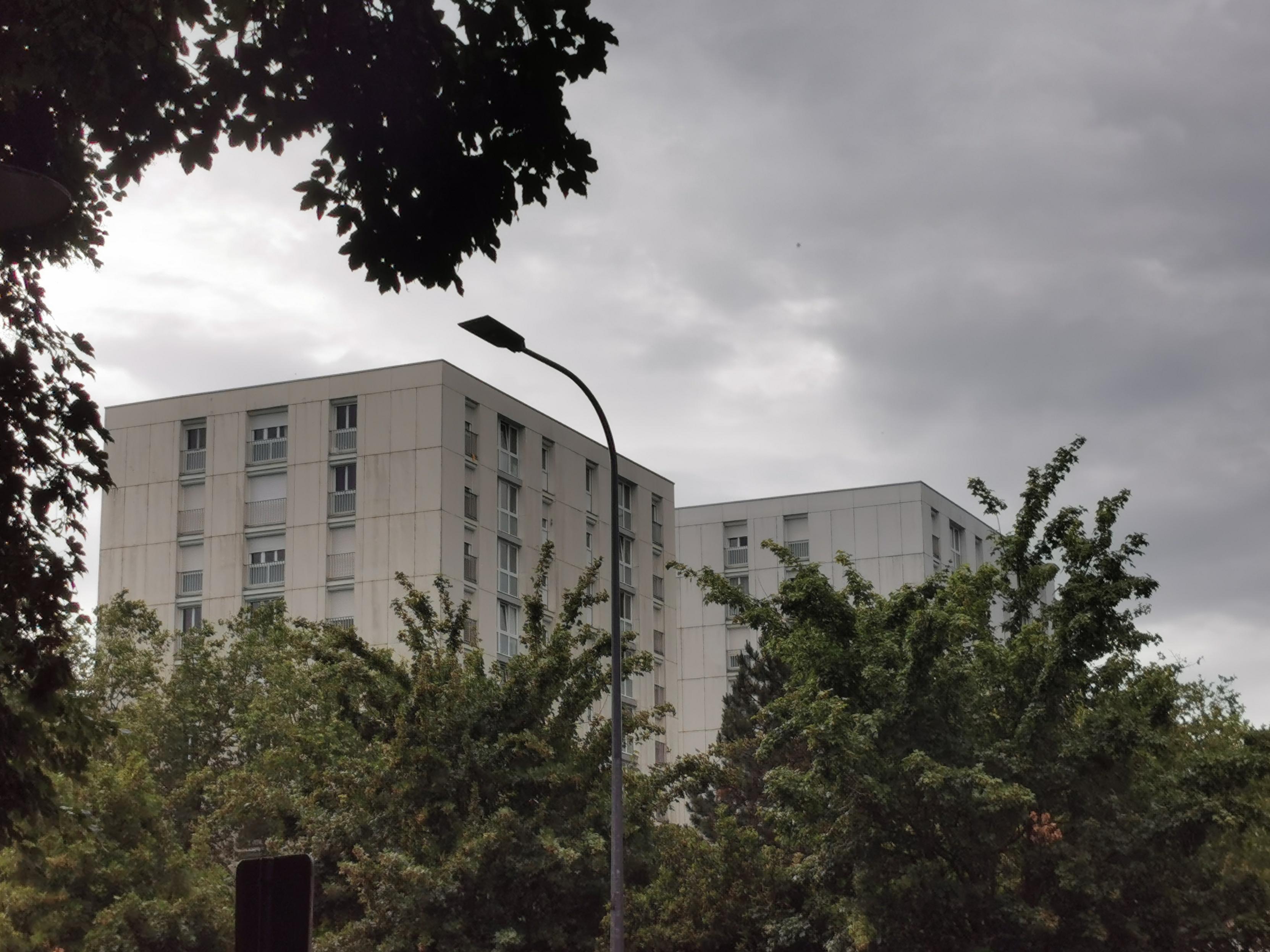 Blocs résidentiels entourés de végétation sous un ciel menaçant.