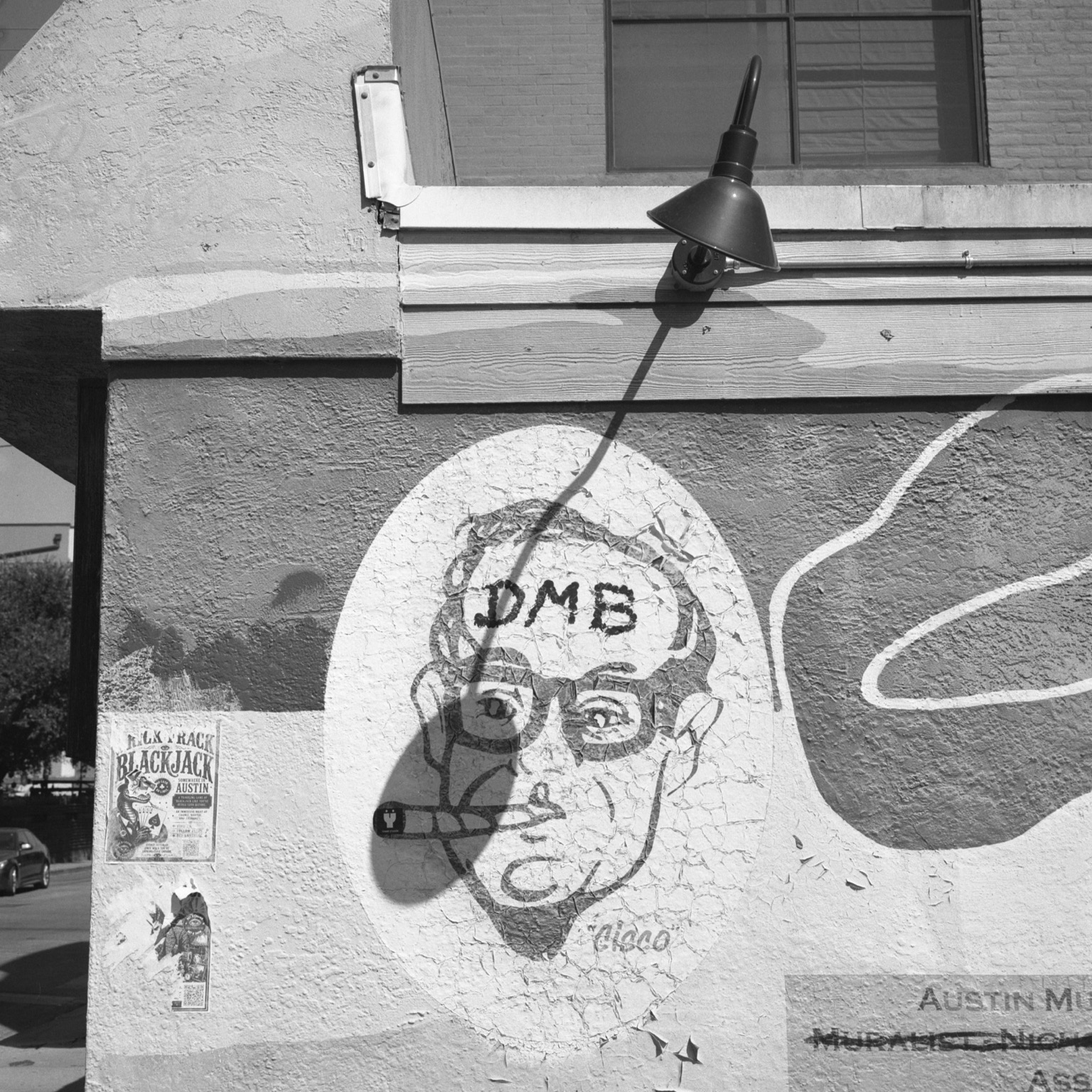 A black-and-white film photo. The shadow from an outdoor lamp partially covers the figure of a man’s face on a mural in East Austin, Texas. Monday, August 17, 2026.