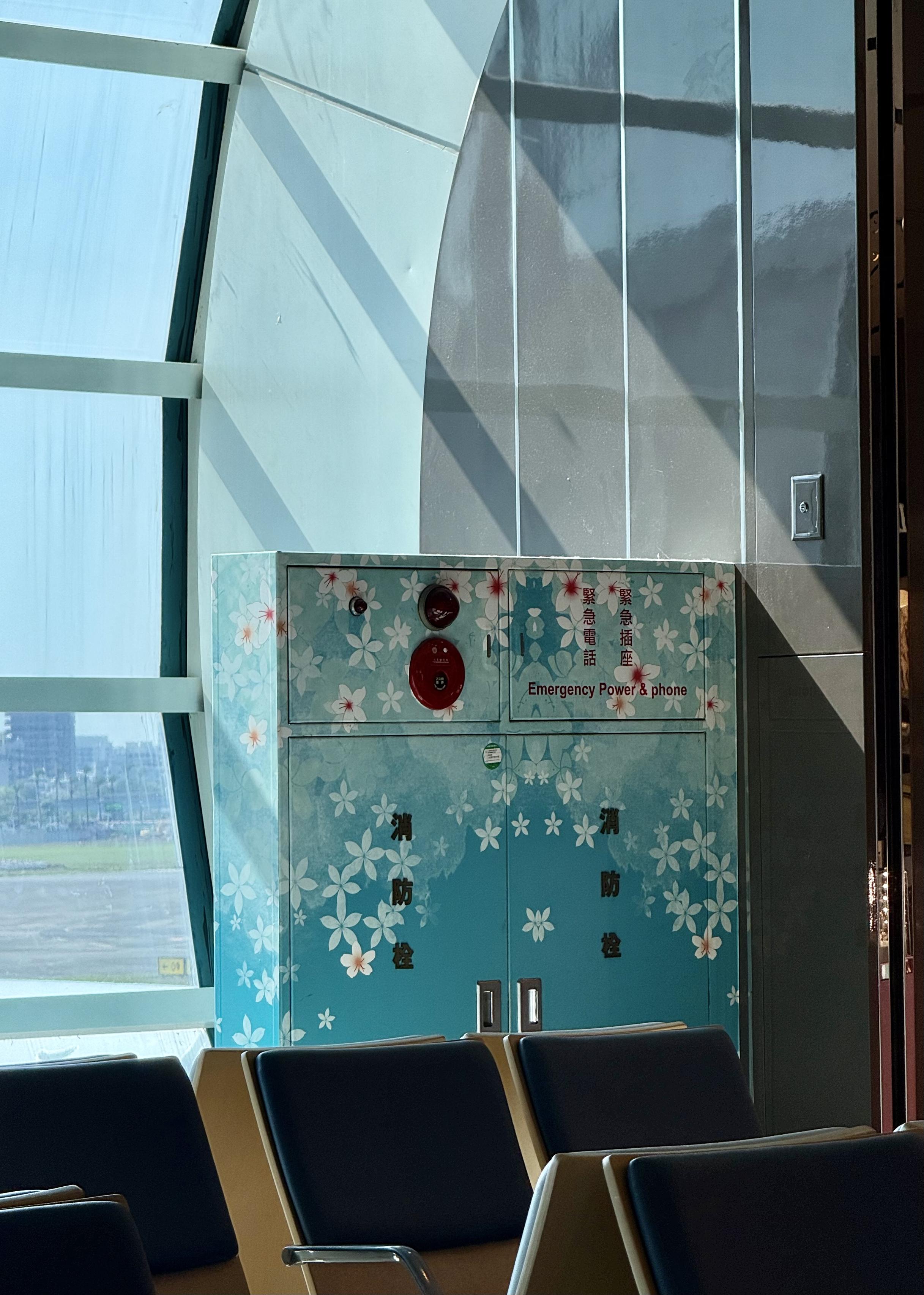 Red emergency power and phone cabinet decorated with white flowers, located in a room with black and yellow chairs.