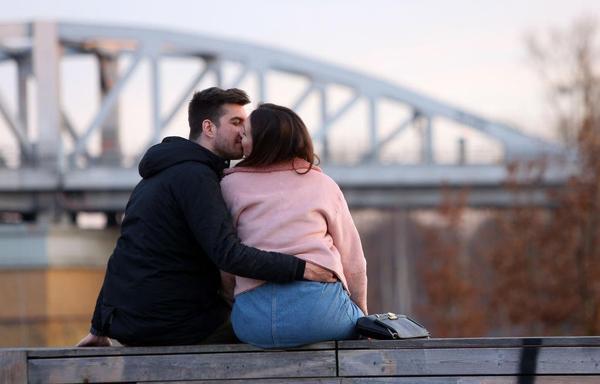 Man and woman kiss in front of a blurred out bridge