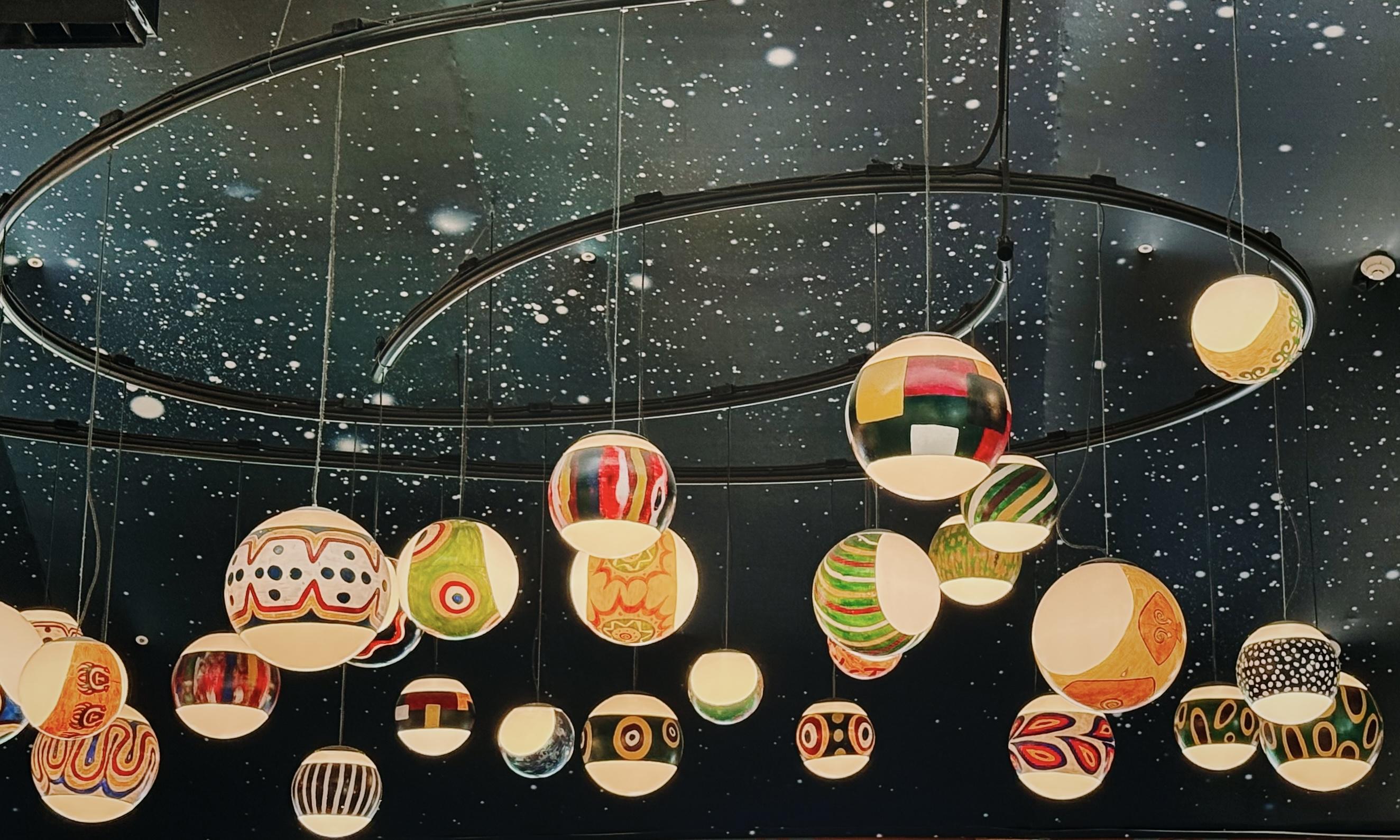 吊灯呈现五彩缤纷的球状灯饰，悬挂于星空般的黑色天花板上。
