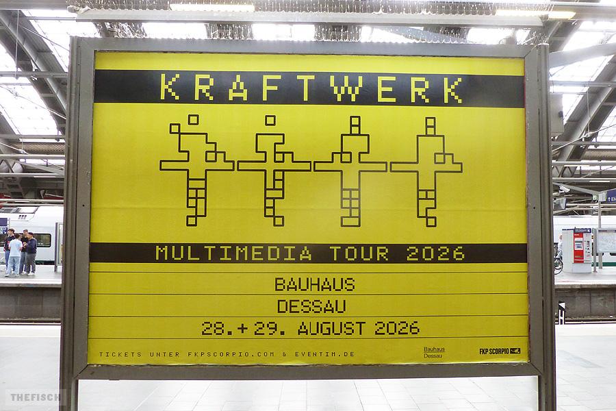 Ein Großplakat wirbt für zwei Konzerte der Band Kraftwerk in Dessau im August 2026. Farben: Schwarz auf Gelb.