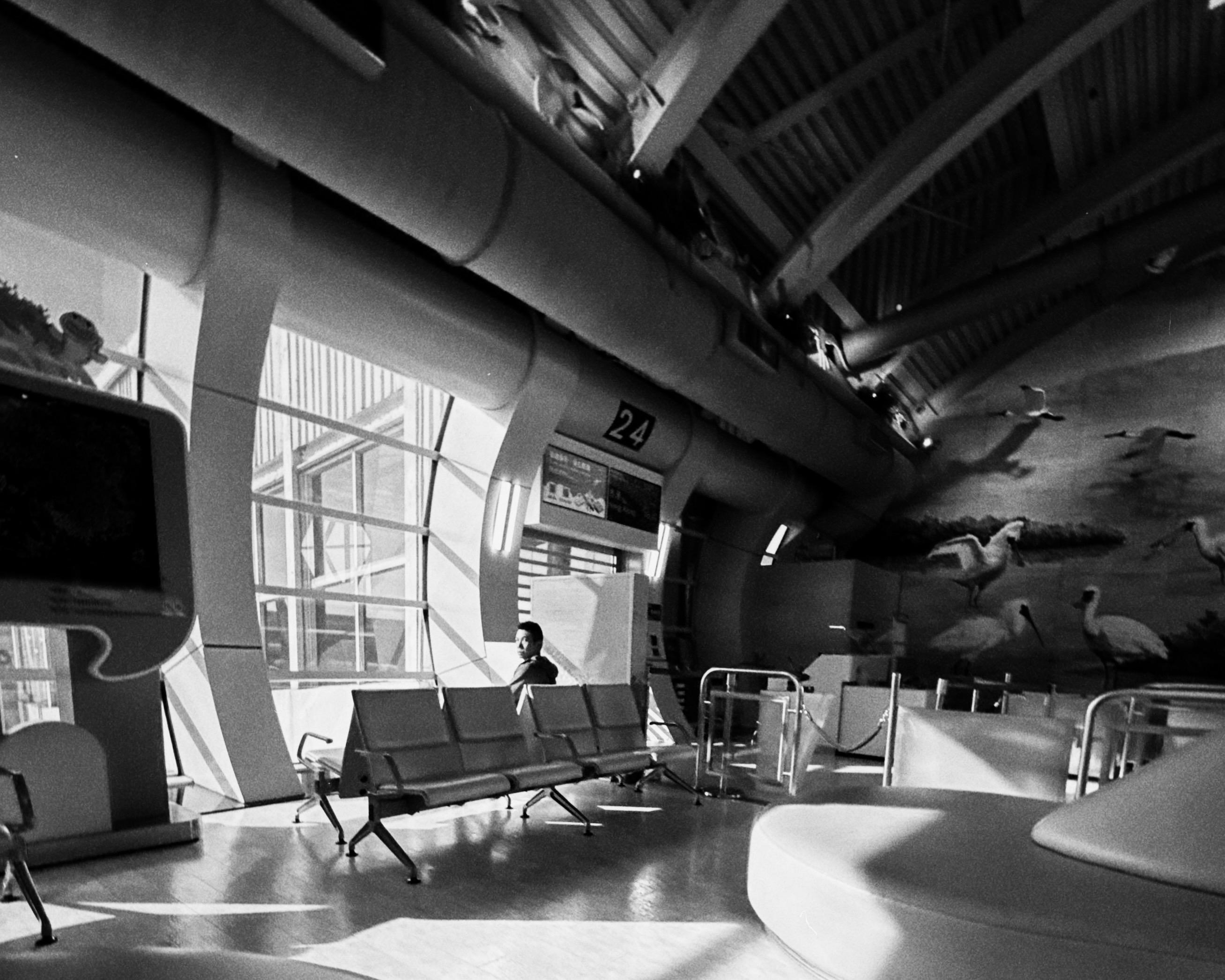 Empty airport terminal with a person sitting on a bench, seating area, and aircraft murals on the wall.