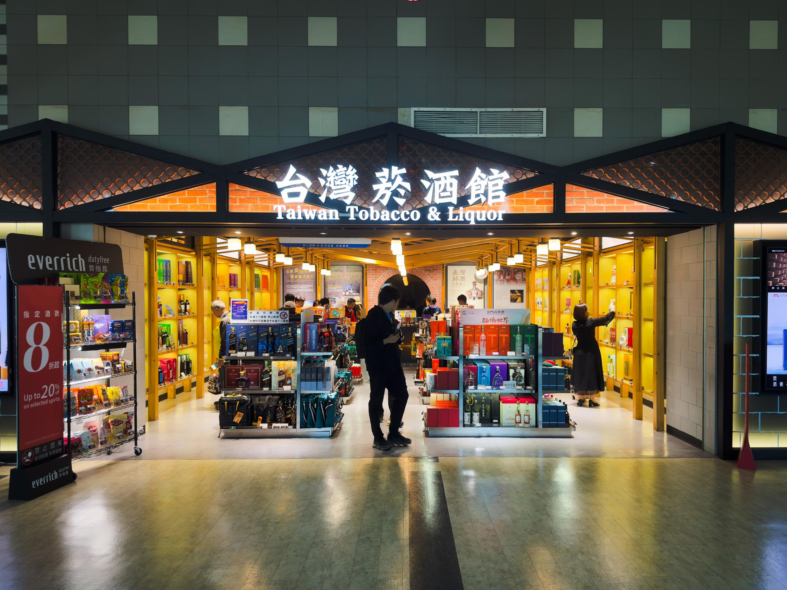 台湾菸酒館，販售台灣煙酒和相關商品，店內明亮且熱鬧，有多位顧客在購買。