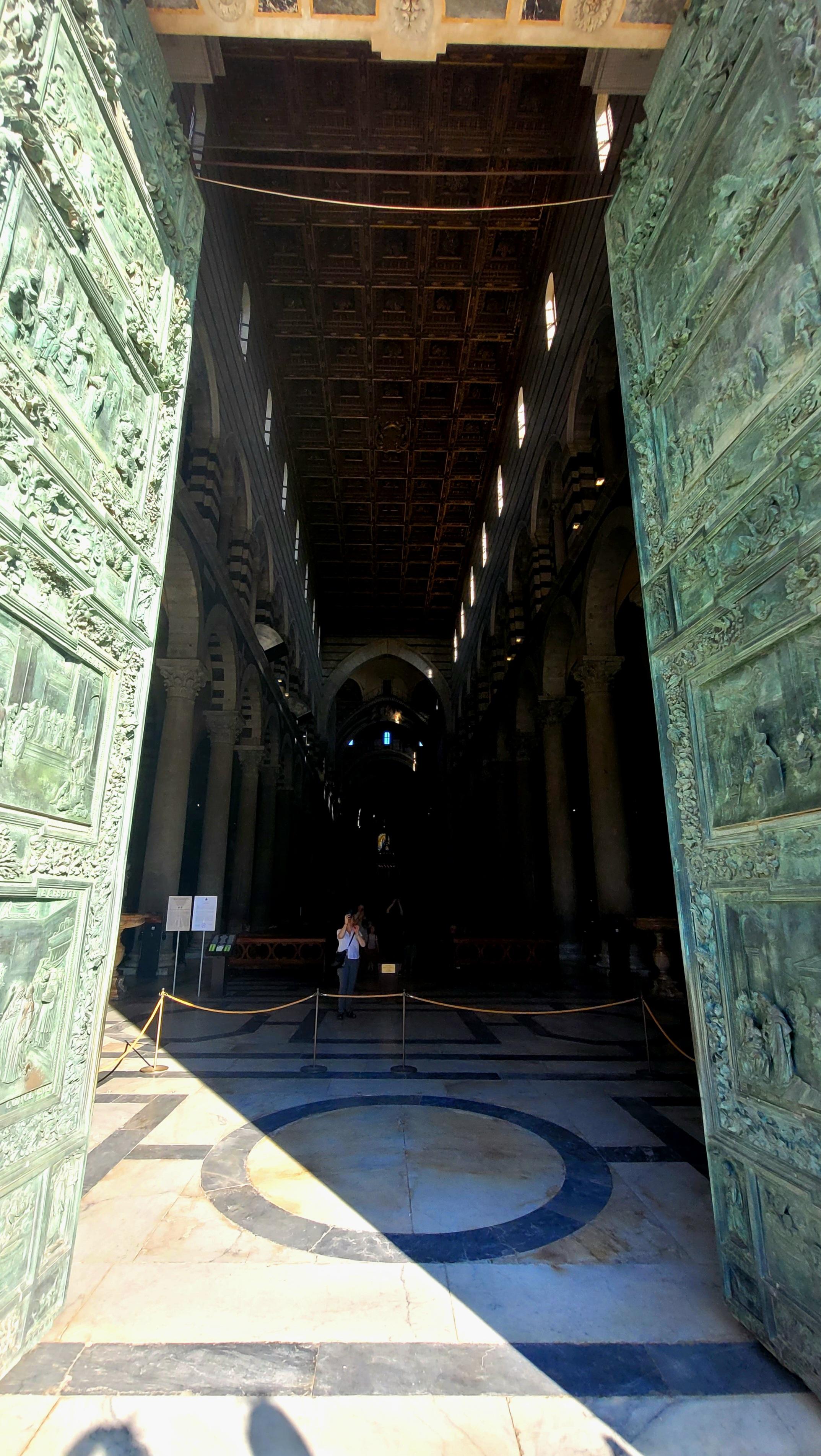 Das geöffnete Bronzeportam am Dom von Pisa lässt einen Blick ins Innere des Doms zu. Der Dom Santa Maria Assunta in Pisa ist das zentrale Meisterwerk der berühmten Piazza dei Miracoli und gilt als eines der bedeutendsten Bauwerke der pisanischen Romanik. Die im 11. Jahrhundert begonnene Kathedrale fasziniert durch ihre Fassade aus weißem Carrara-Marmor und diente jahrhundertelang als architektonisches Vorbild für spätere Großbauten in ganz Italien. Toskana 2025