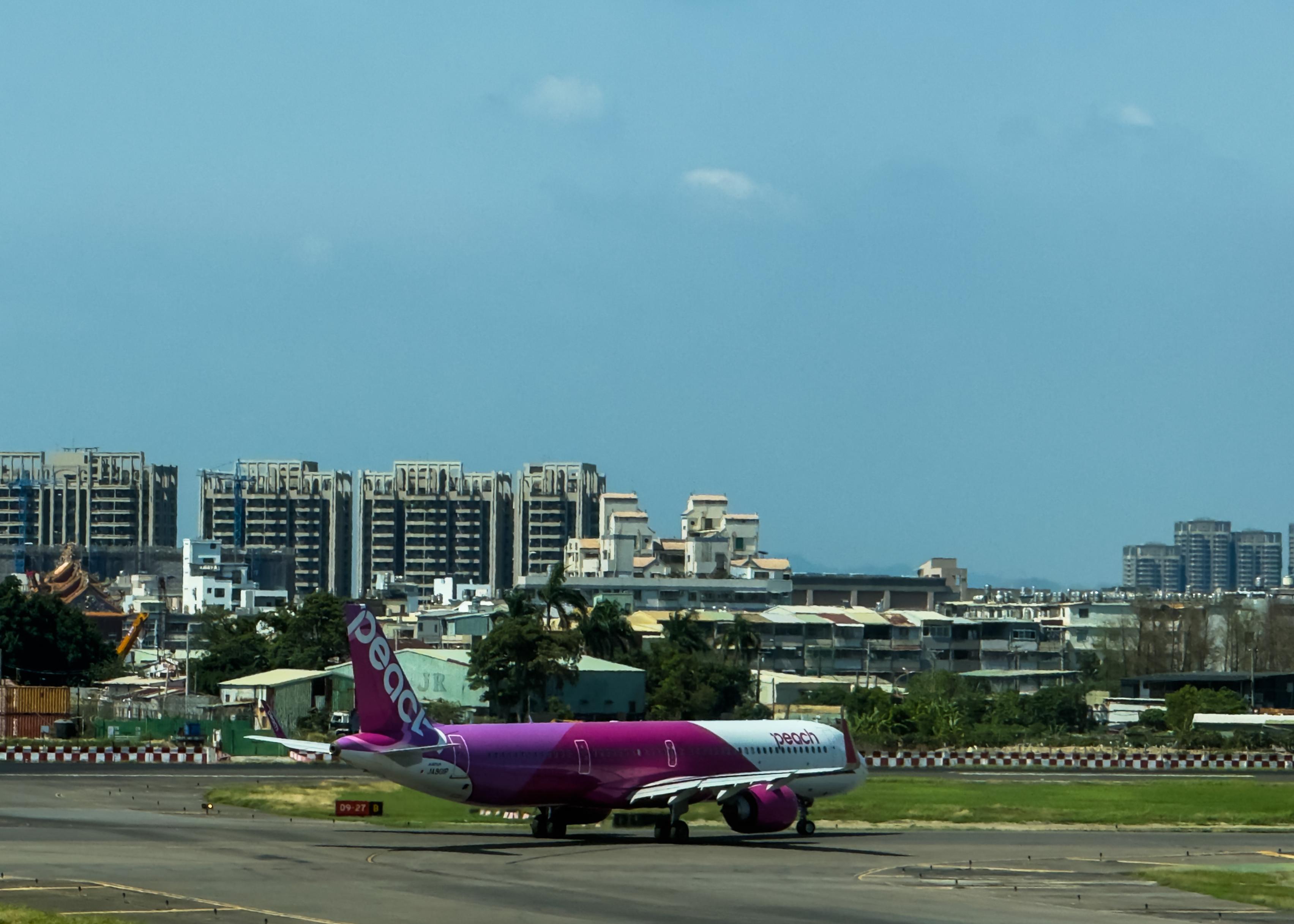 A Peacy Airlines plane on the runway with tall buildings and a blue sky in the background.