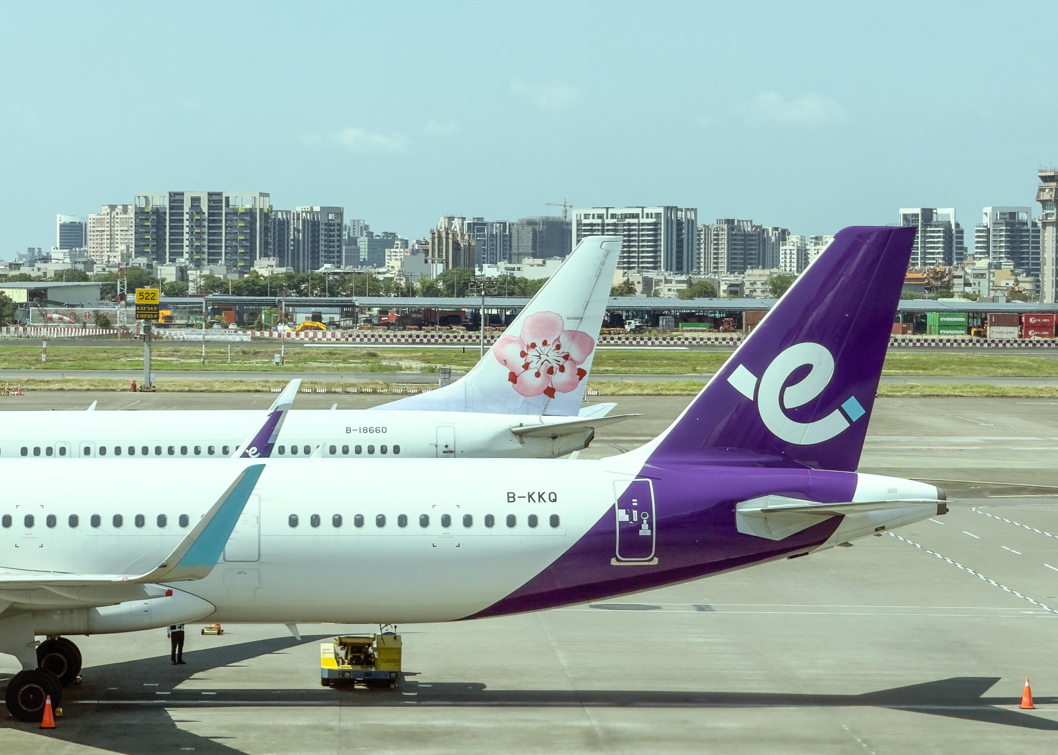 机场停机坪上的两架飞机尾部，美国航空和泰国优步飞机，背景是城市天际线。