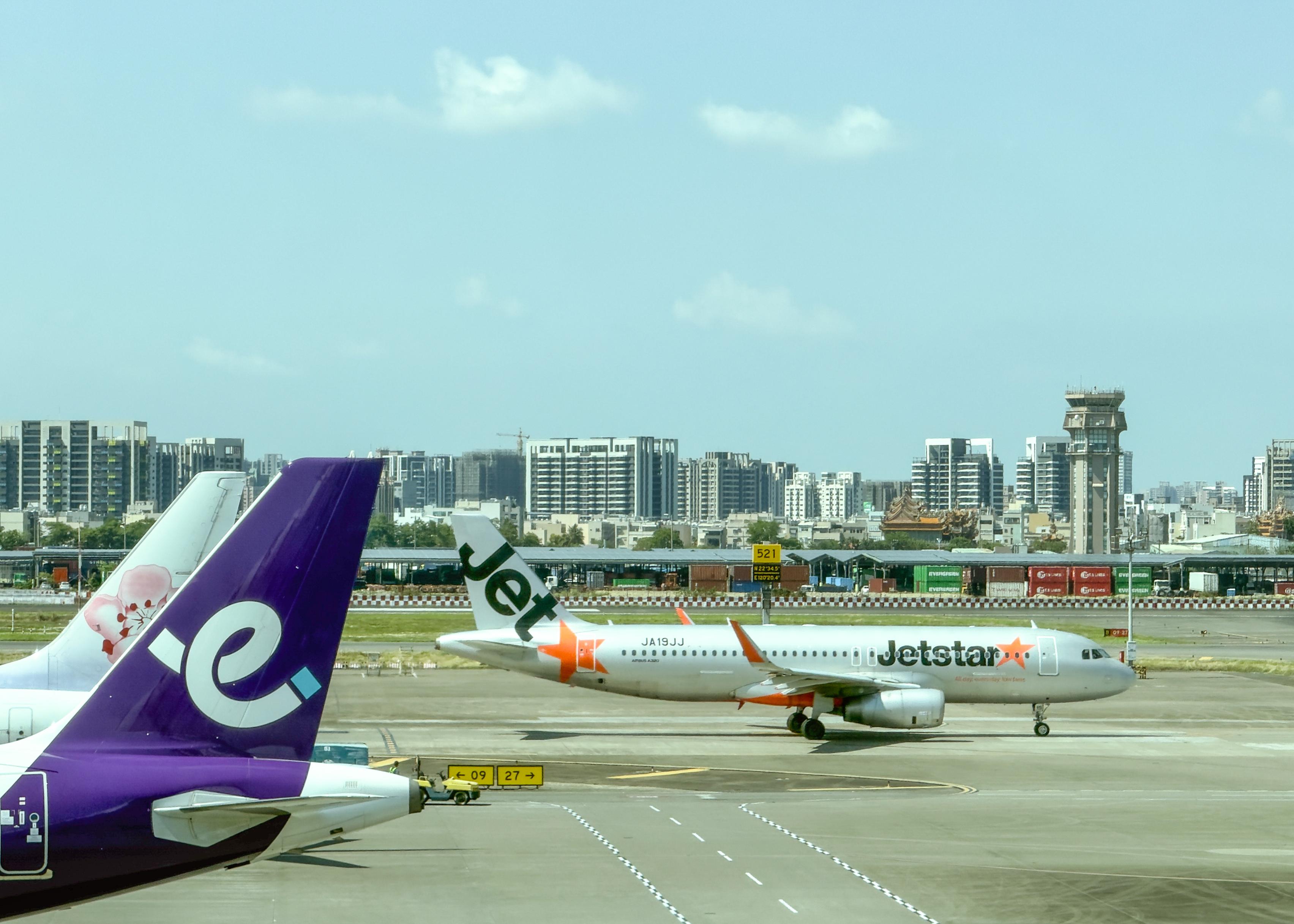 机场跑道上有两架飞机，一架Jetstar和另一架Jet的尾翼在机场跑道上。