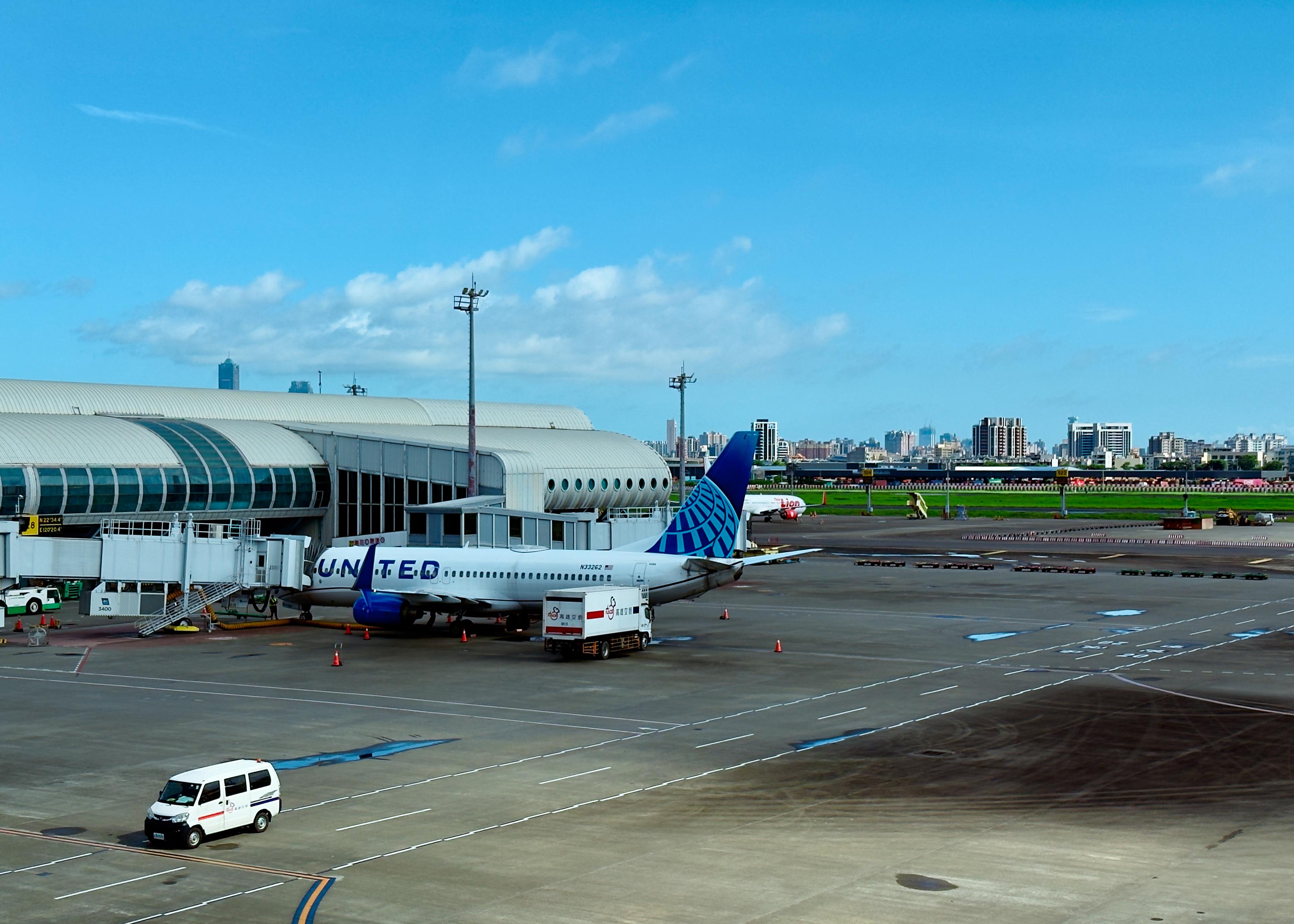 国际机场的停机区，一架联合航空飞机停靠在登机口旁，城市天际线在远处可见。