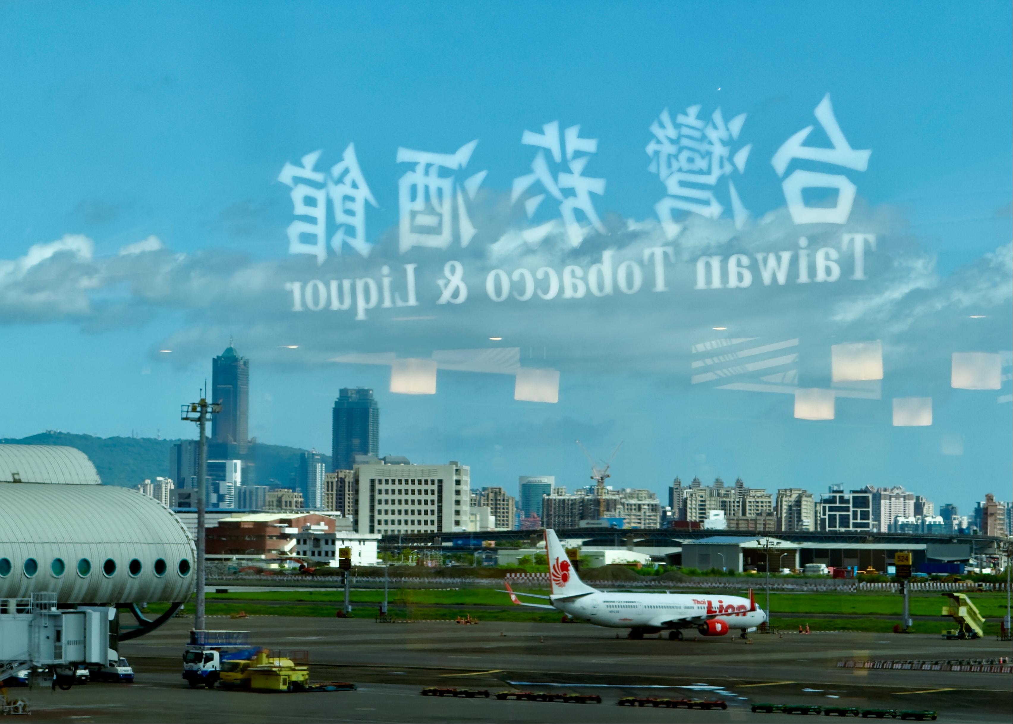 透过机场窗户看到飞机和城市天际线，玻璃上的文字反映出“Truwan Tobacco & Liquor”。