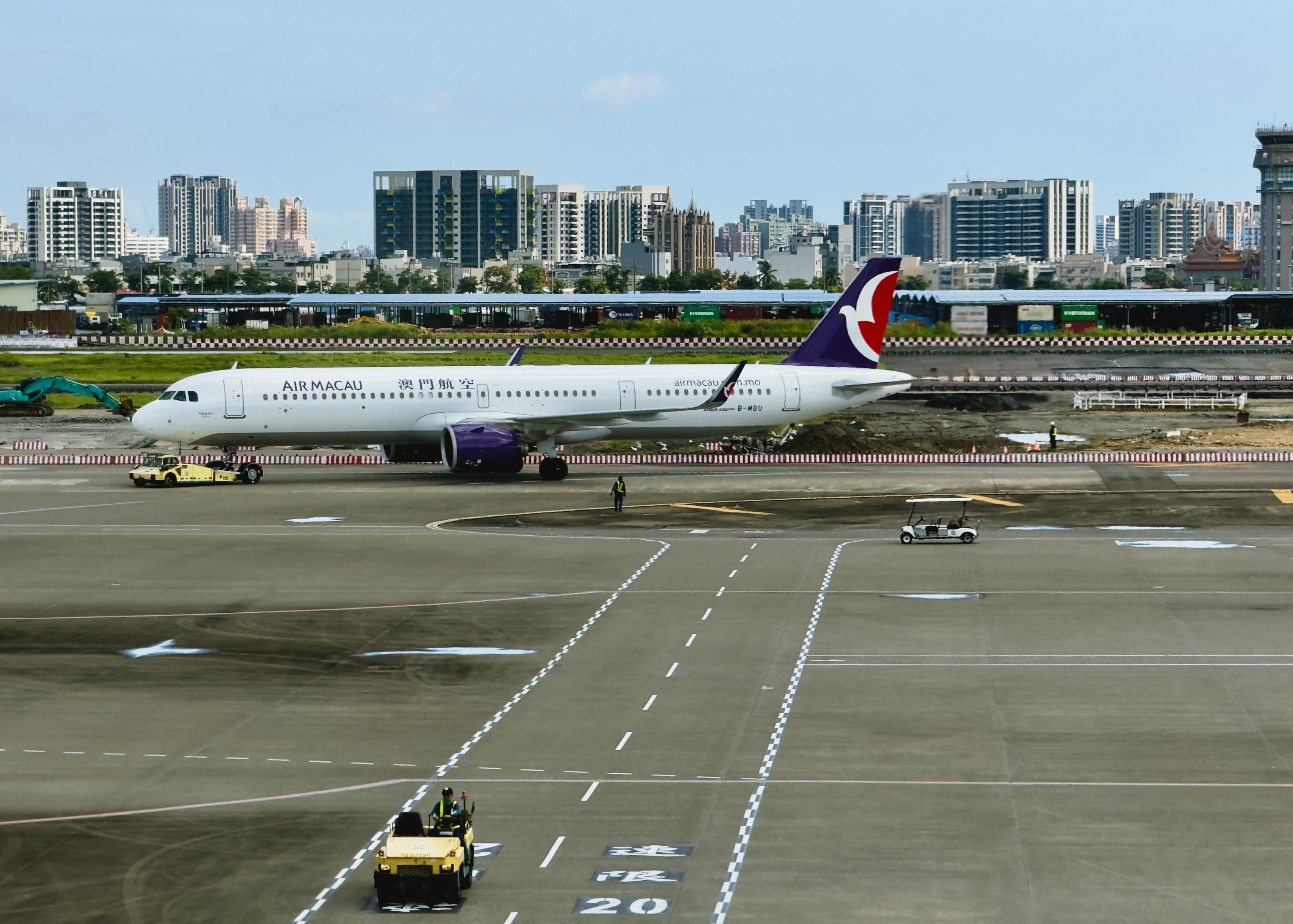 澳门航空飞机在机场跑道上待命，背景是城市高楼。