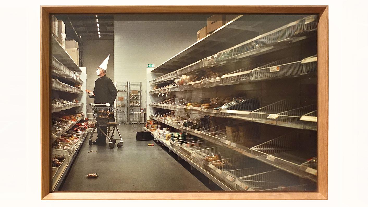 Een foto uit de serie April Fool uit 2020. In een gangpad van een supermarkt staat Erwin Olaf als een clown met een wit puntmuts en een wit gezicht en een zwarte jas te kijken naar de overgebleven producten in de schappen. Erwin heeft een product in zijn hand. De supermarkt lijkt te zijn leeggeroofd. Enkele producten liggen. op de grond. Het geheel is verontrustend. Dit beeld appelleert aan consumptisme. Kopen, kopen ten koste van alles, iedereen en de wereld. De kleur van de foto is vrij neutraal. Hierdoor wordt de sfeer nog extra bedompt.
