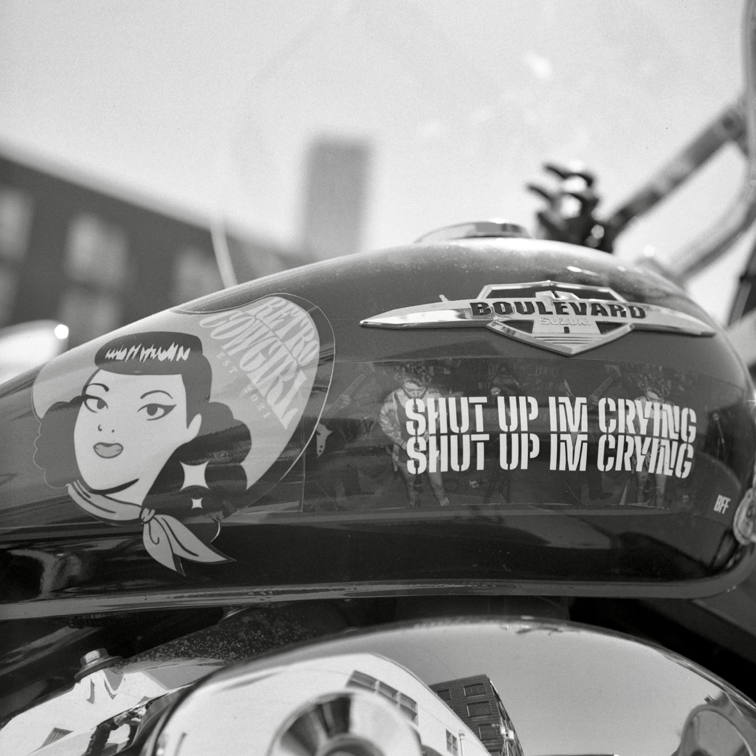 A black-and-white film photo. Stickers adorn a motorcycle gas tank in East Austin, Texas. Monday, August 17, 2026.