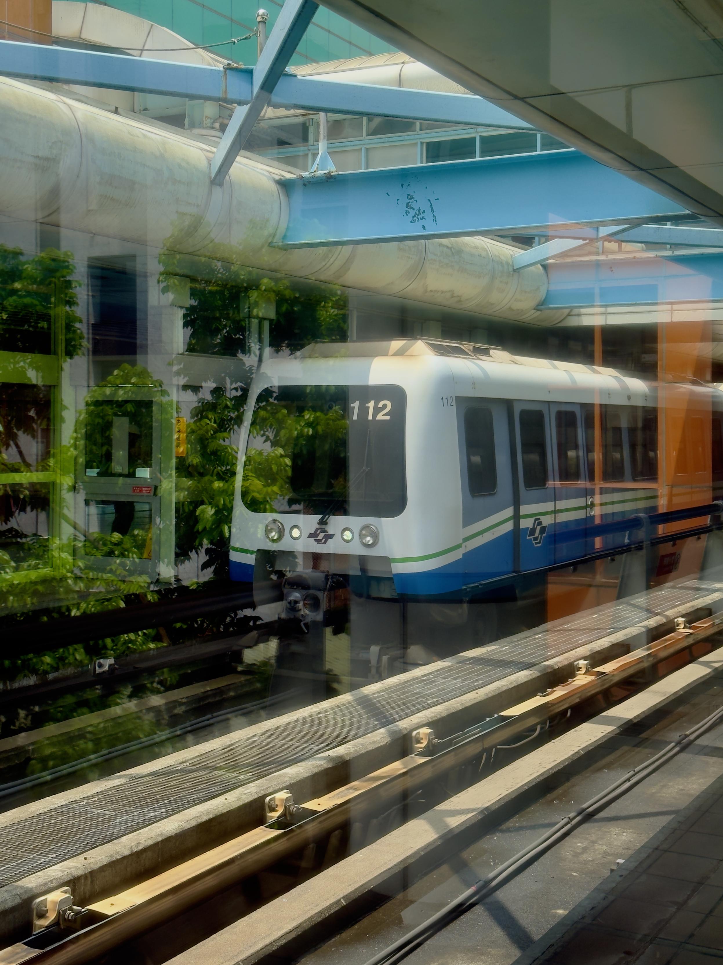 地铁列车经过城市轨道，看得见从玻璃窗反射的街道和绿树。