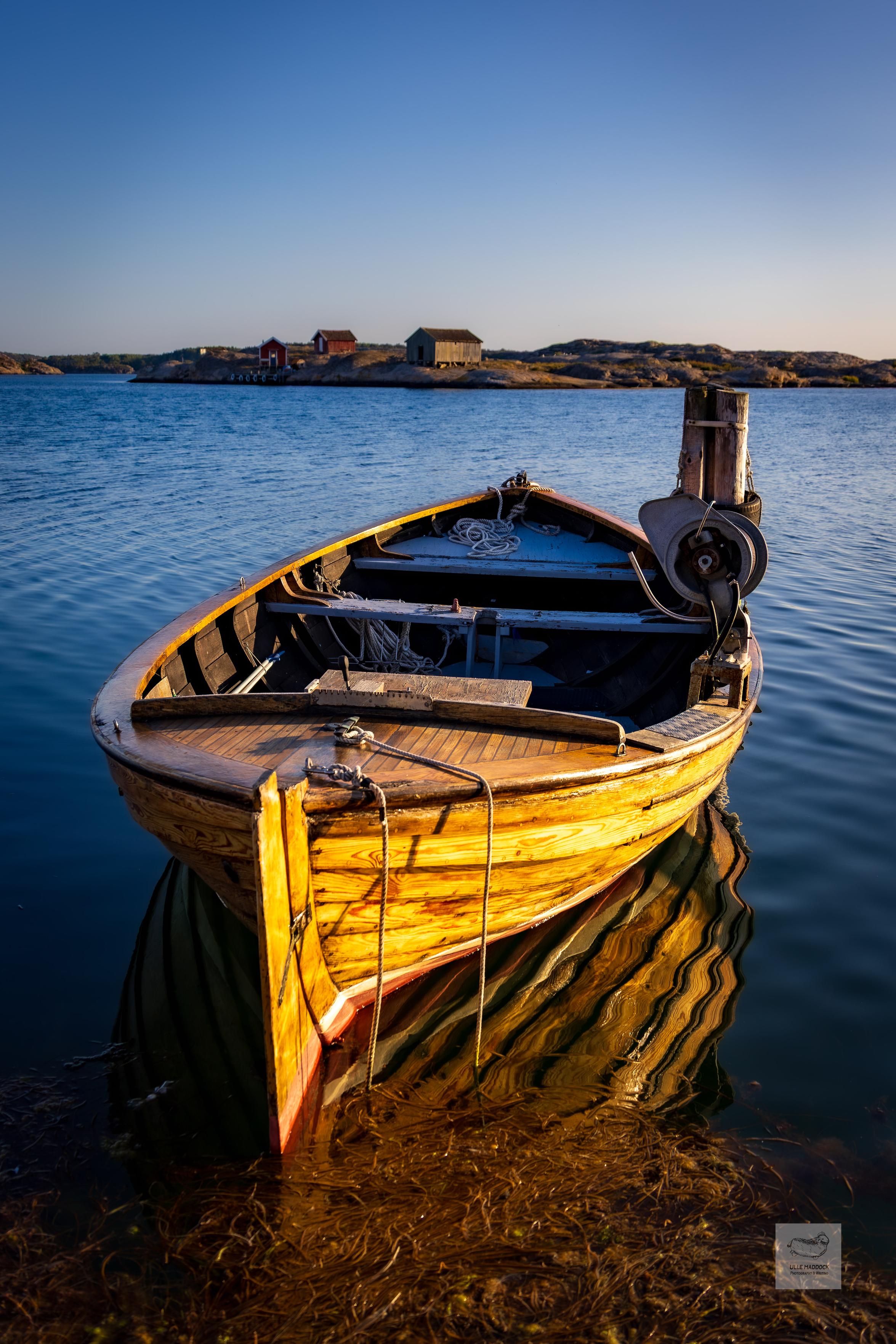 Old wooden boat with boat sheds in distance.