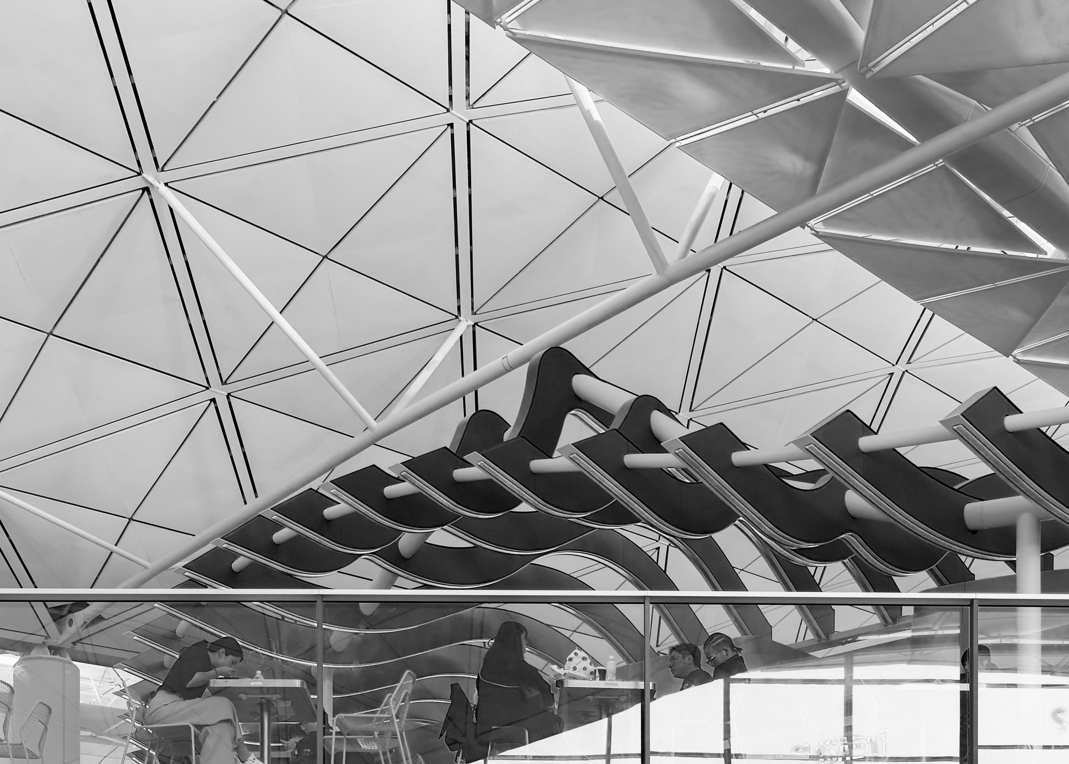 People sitting at outdoor tables under a modern, geometric building structure.