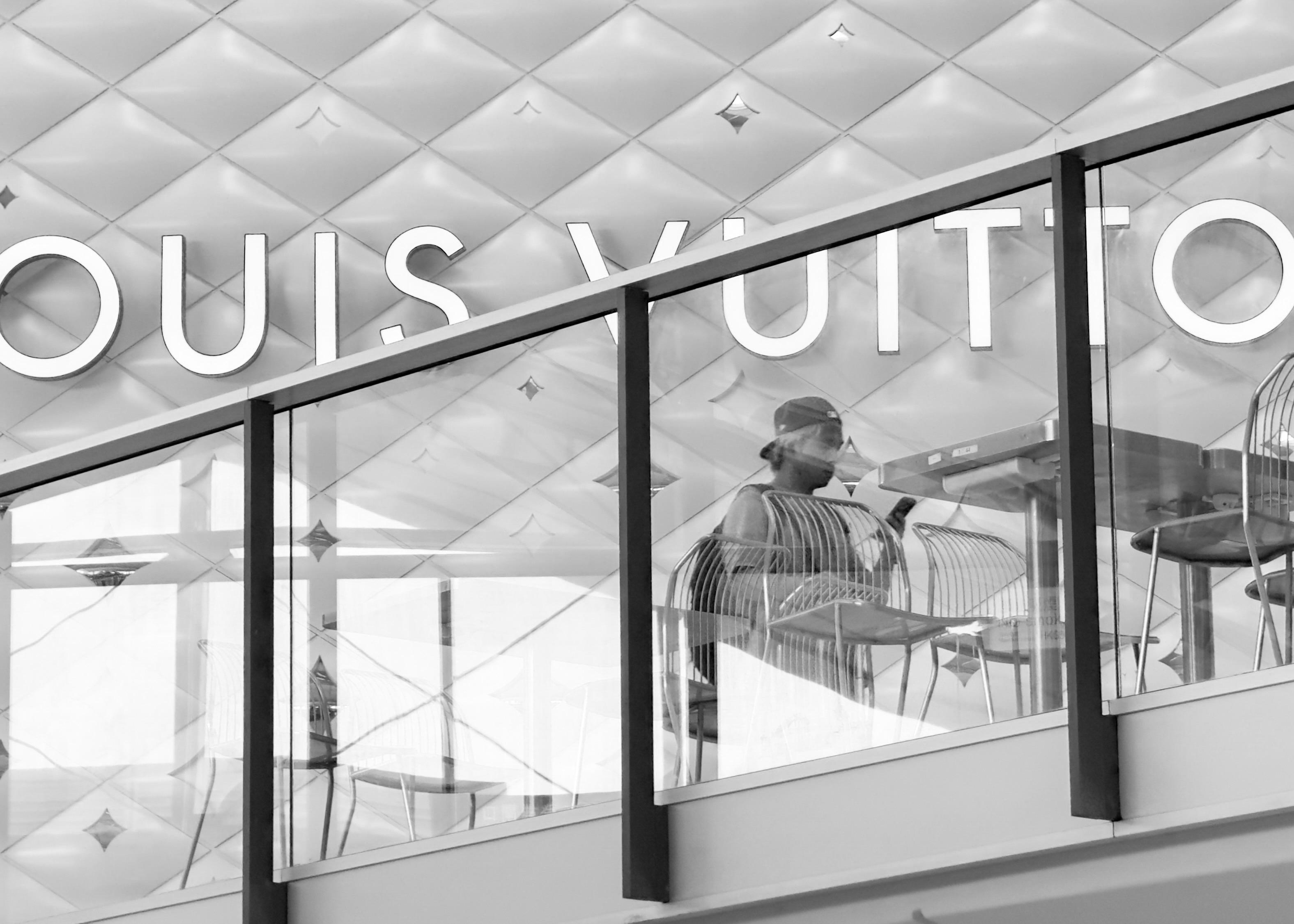 A person sitting inside a Louis Vuitton store, looking at their phone, with store signage visible in the background.