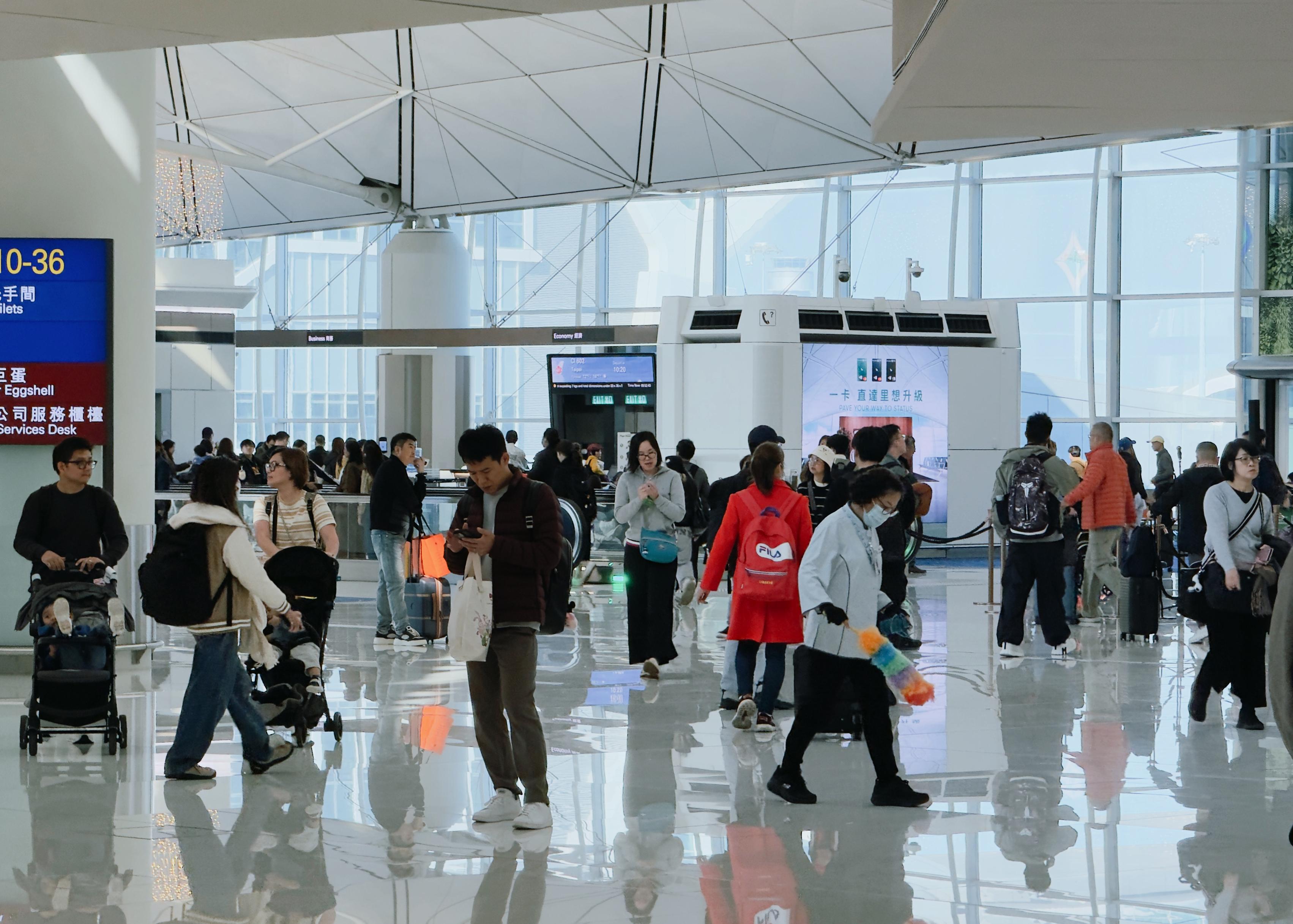 Crowd of travelers with luggage and carts inside an airport terminal, with glass walls and high ceilings.