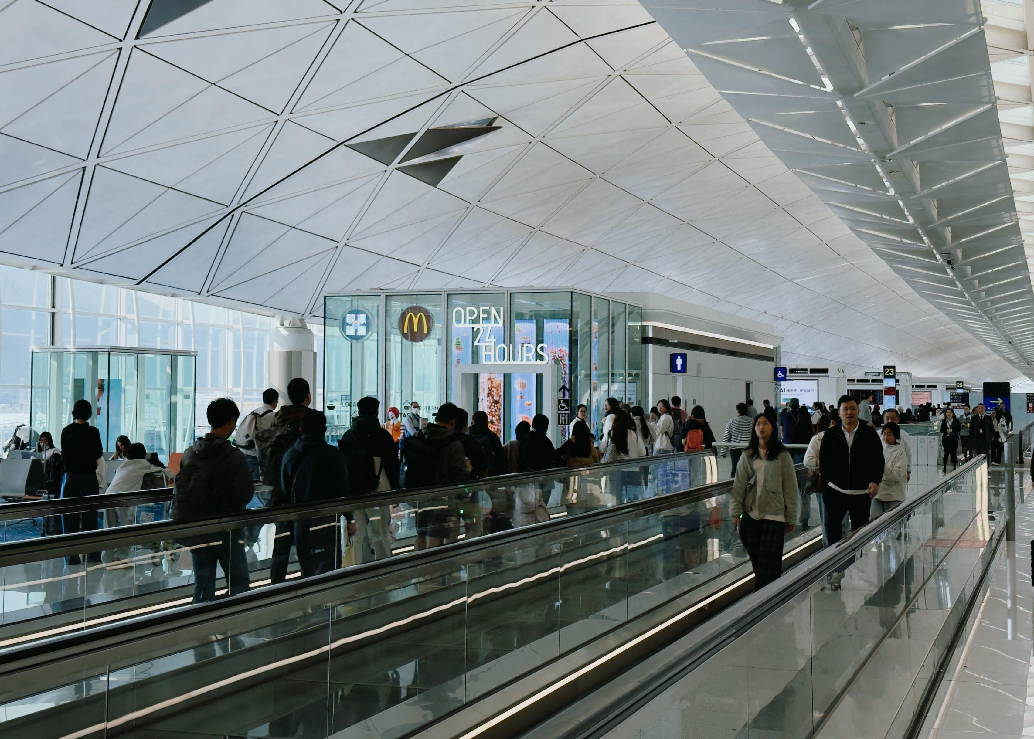 Crowd of travelers walking and waiting at an airport terminal with a McDonald's restaurant in the background.
