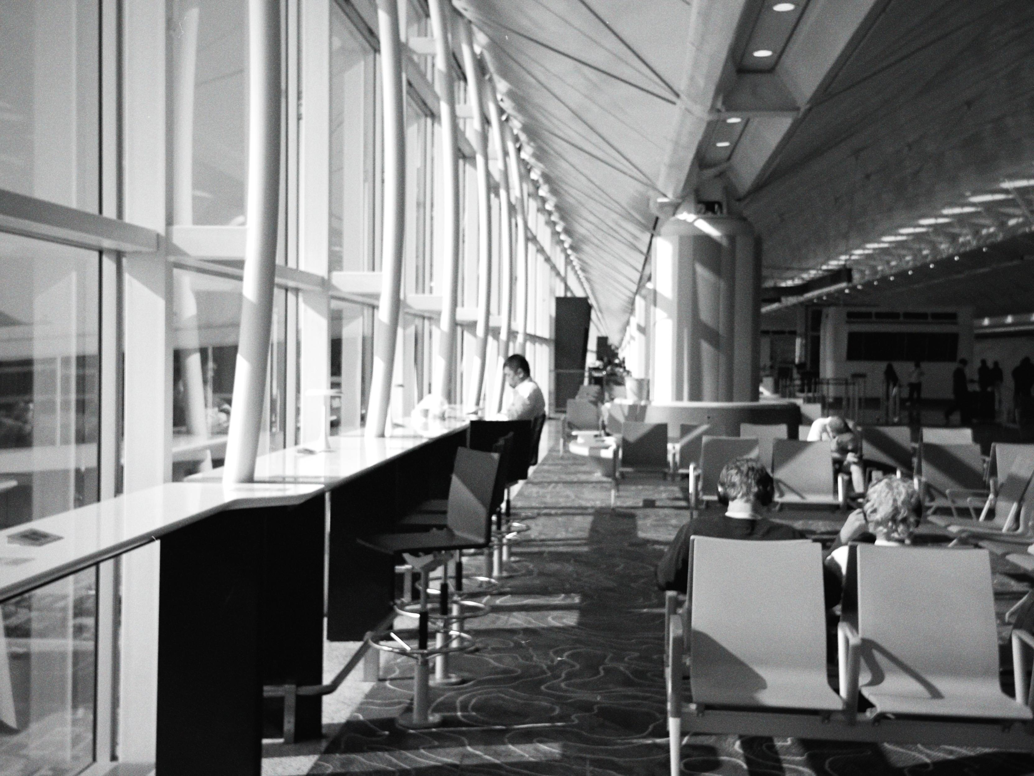 People sitting and waiting in an airport terminal with large windows and modern architecture.