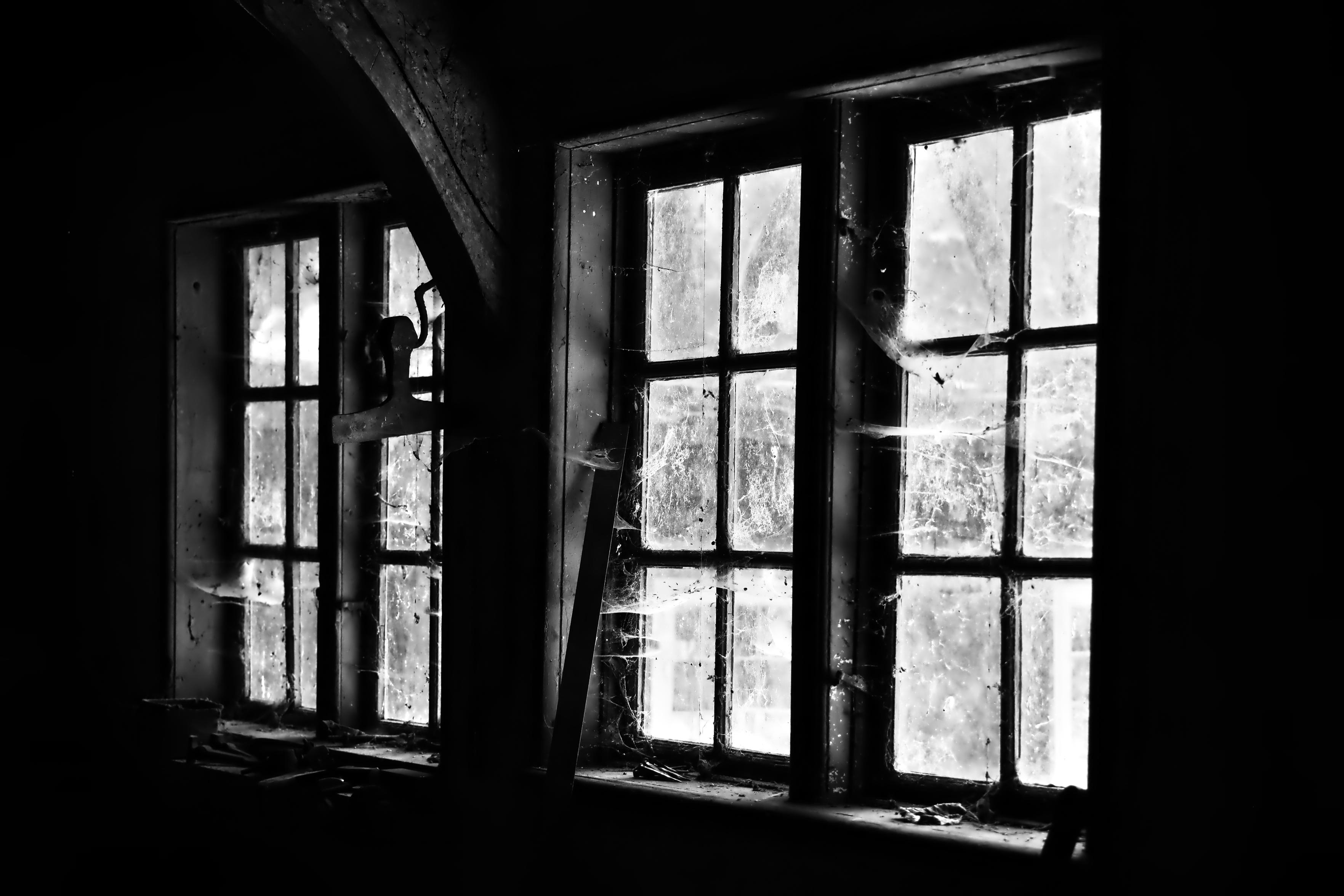 Schwarzweiss-Foto einer kleinen historischen Holzfenster-Front, welche seit längerem nicht mehr gereinigt wurde und mit Spinnenweben und Staub bedeckt ist.