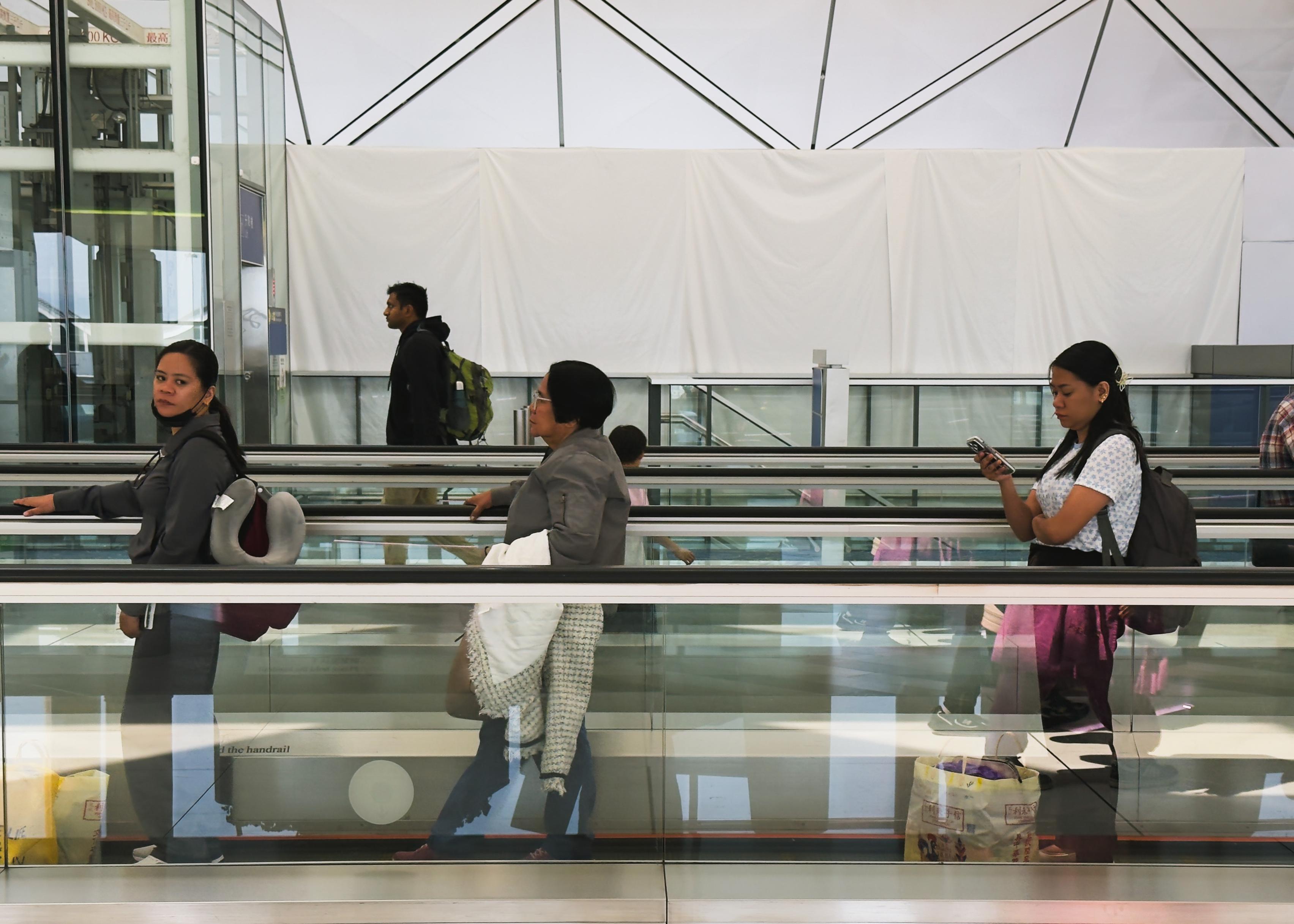 People walking on a moving walkway at an airport terminal.