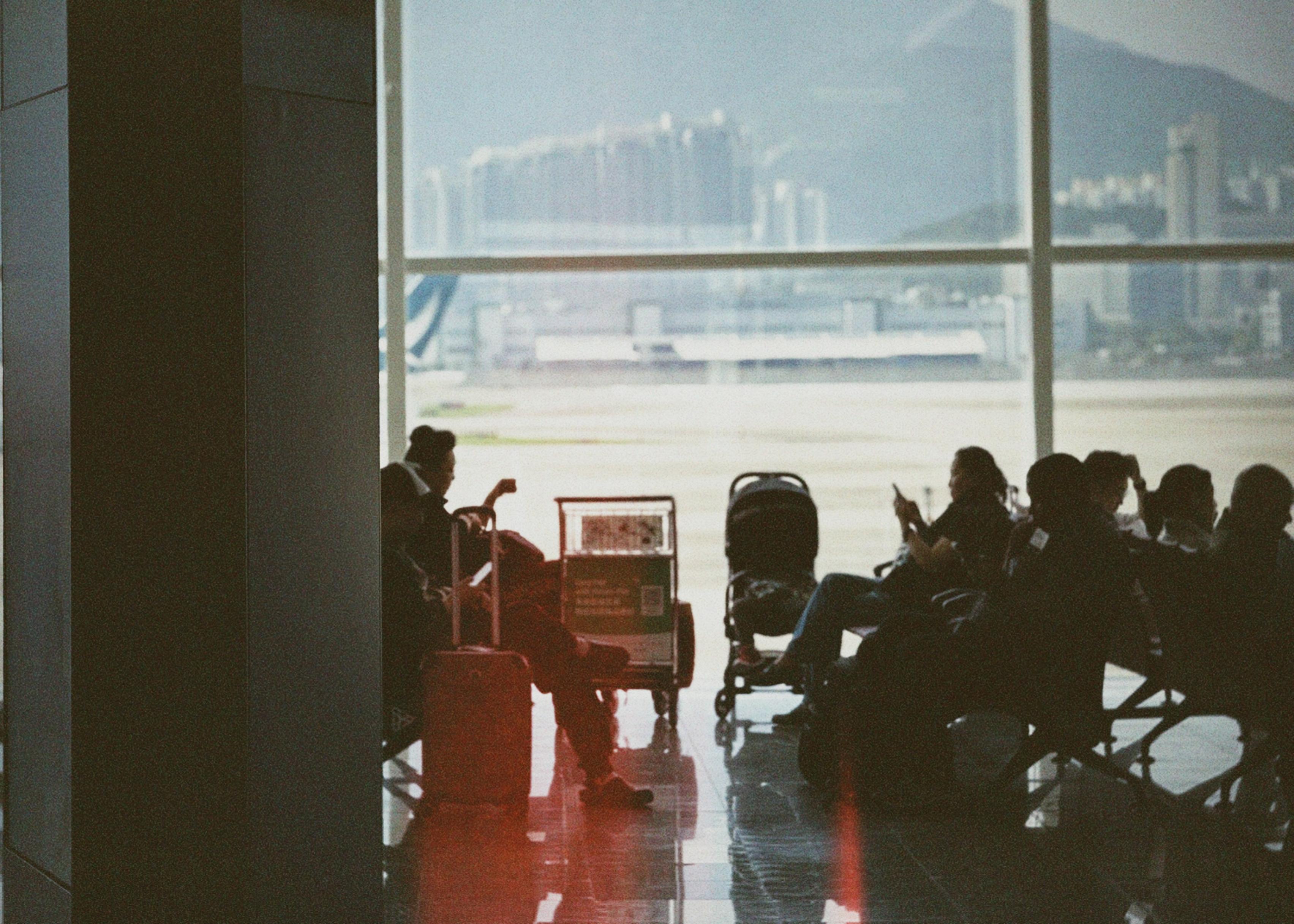 机场候机区，旅客在休息，背后大型玻璃窗外可见城市天际线。