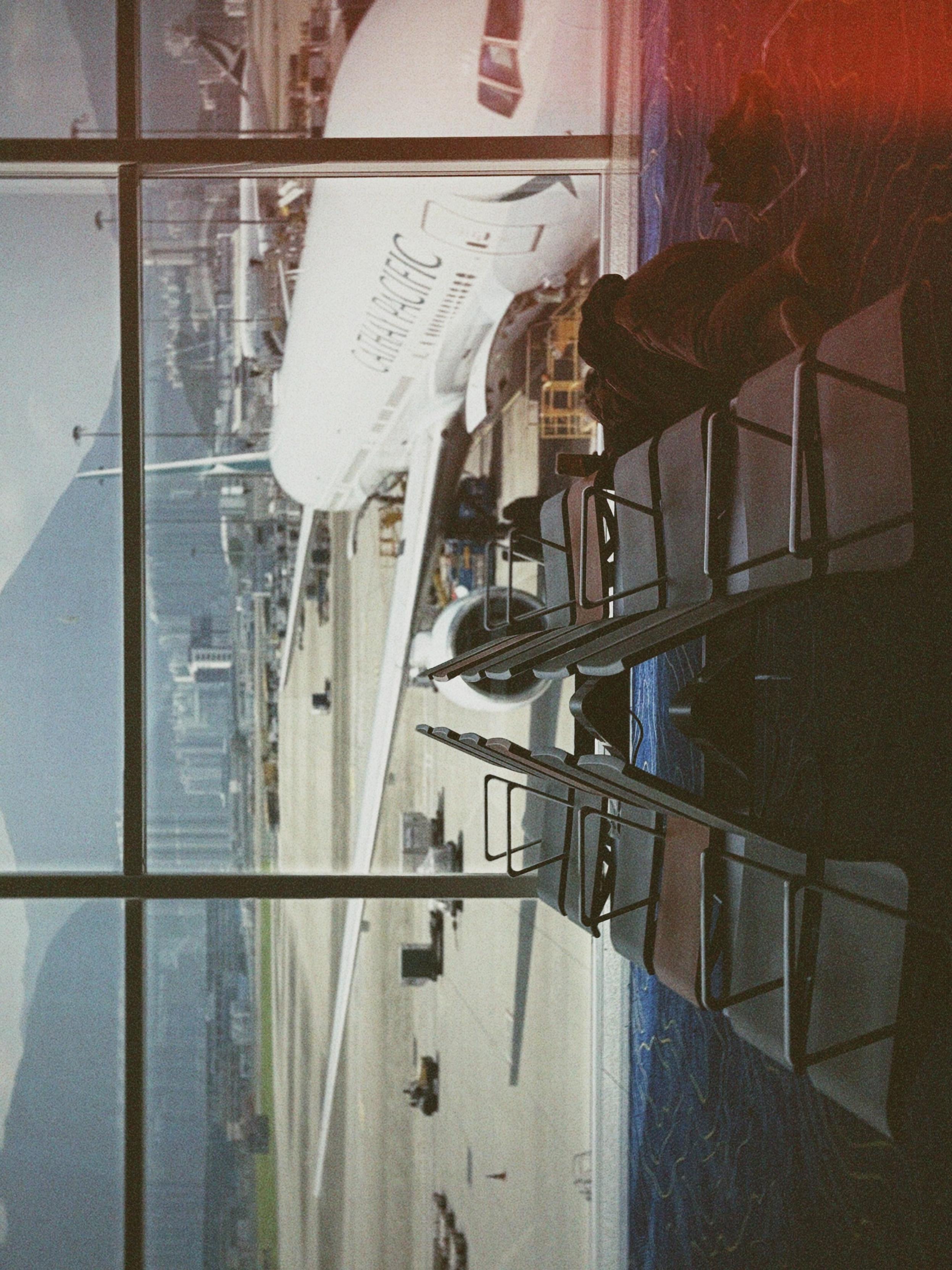Aircraft parked outside through a large window, with empty chairs inside and some passengers waiting.